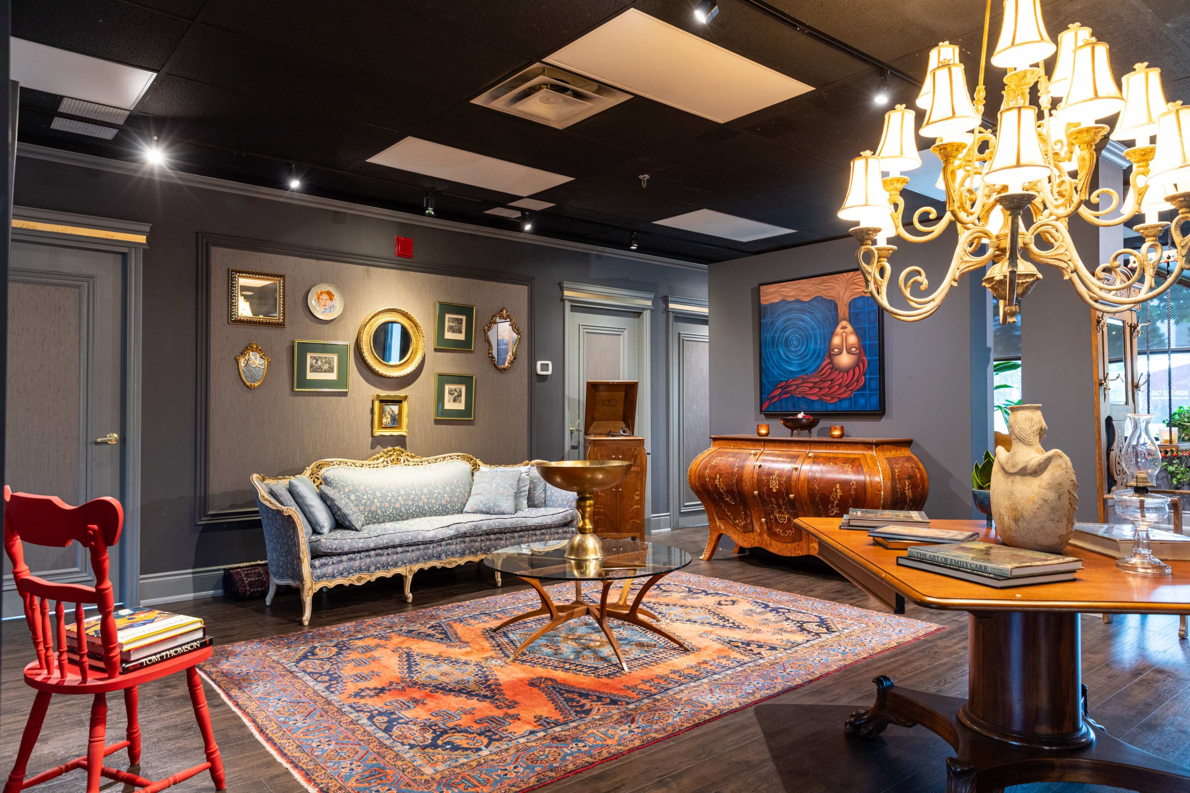 The image shows a stylish interior living space featuring a blue upholstered sofa, a wooden coffee table, and an ornate chandelier, with various artwork and decorative items on the walls.