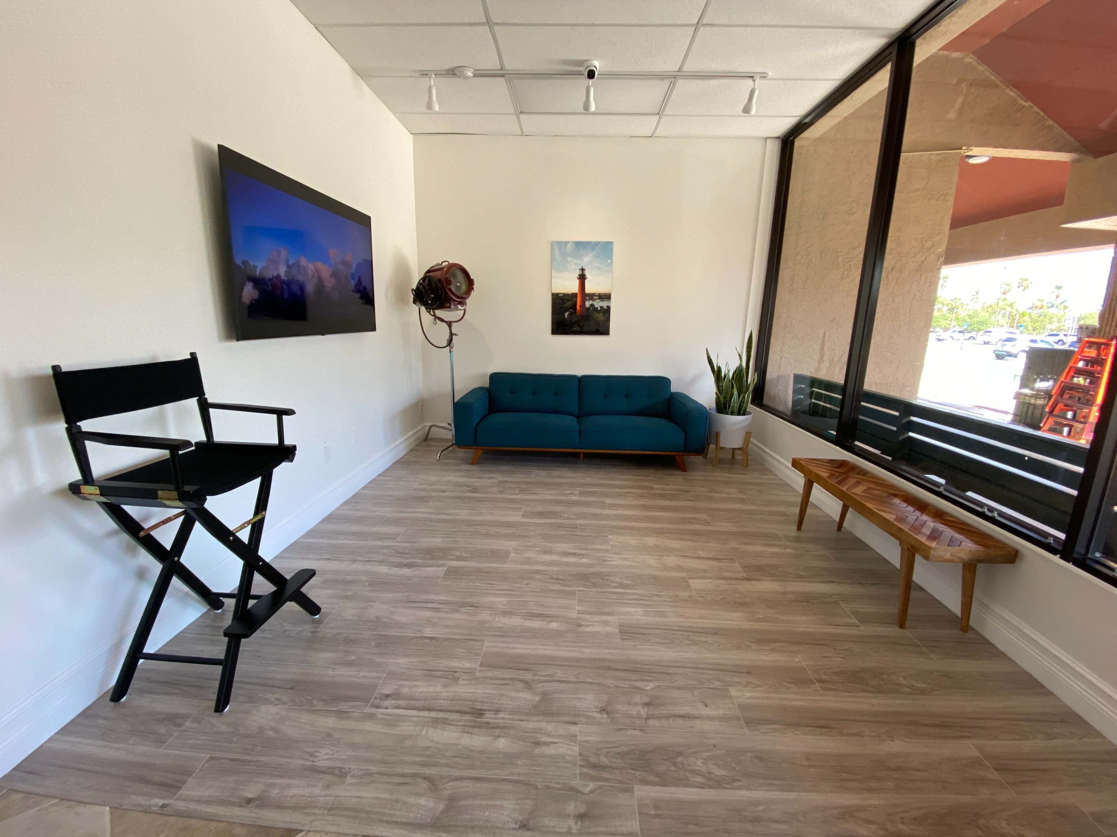 A modern interior space with a turquoise sofa, a wooden table, a director's chair, and a large window providing natural light.