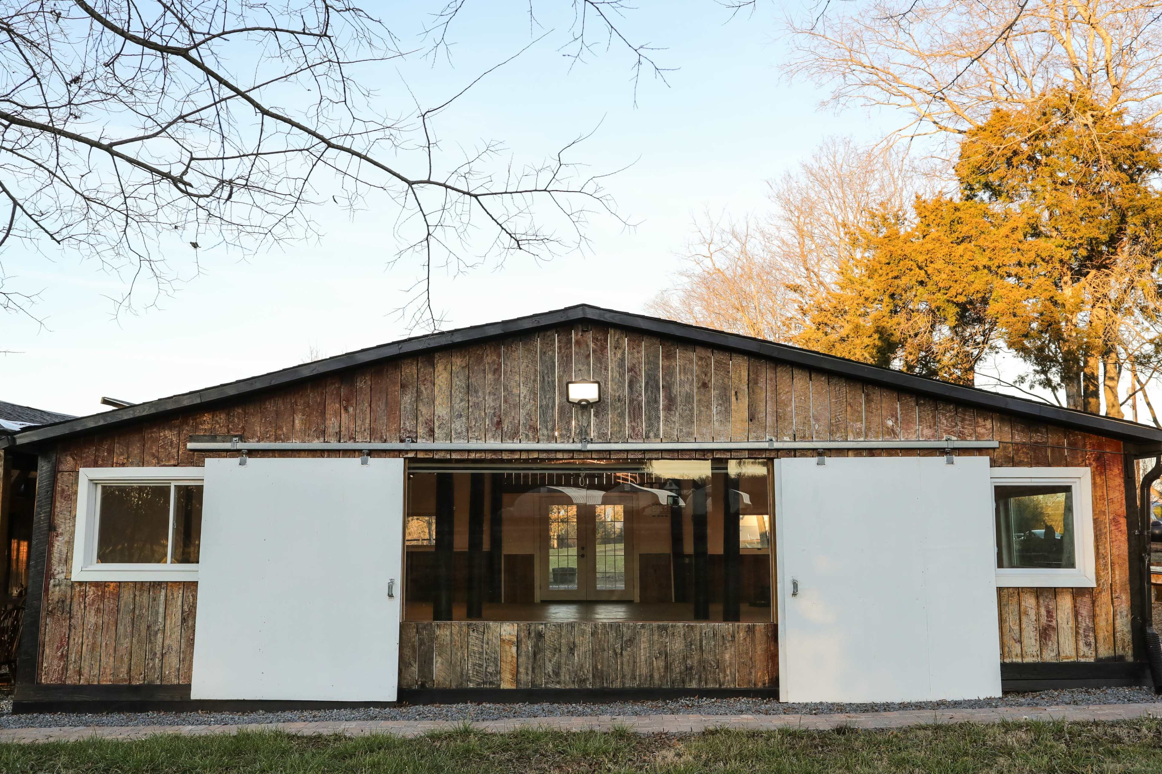 A rustic wooden building with sliding white doors and large windows.