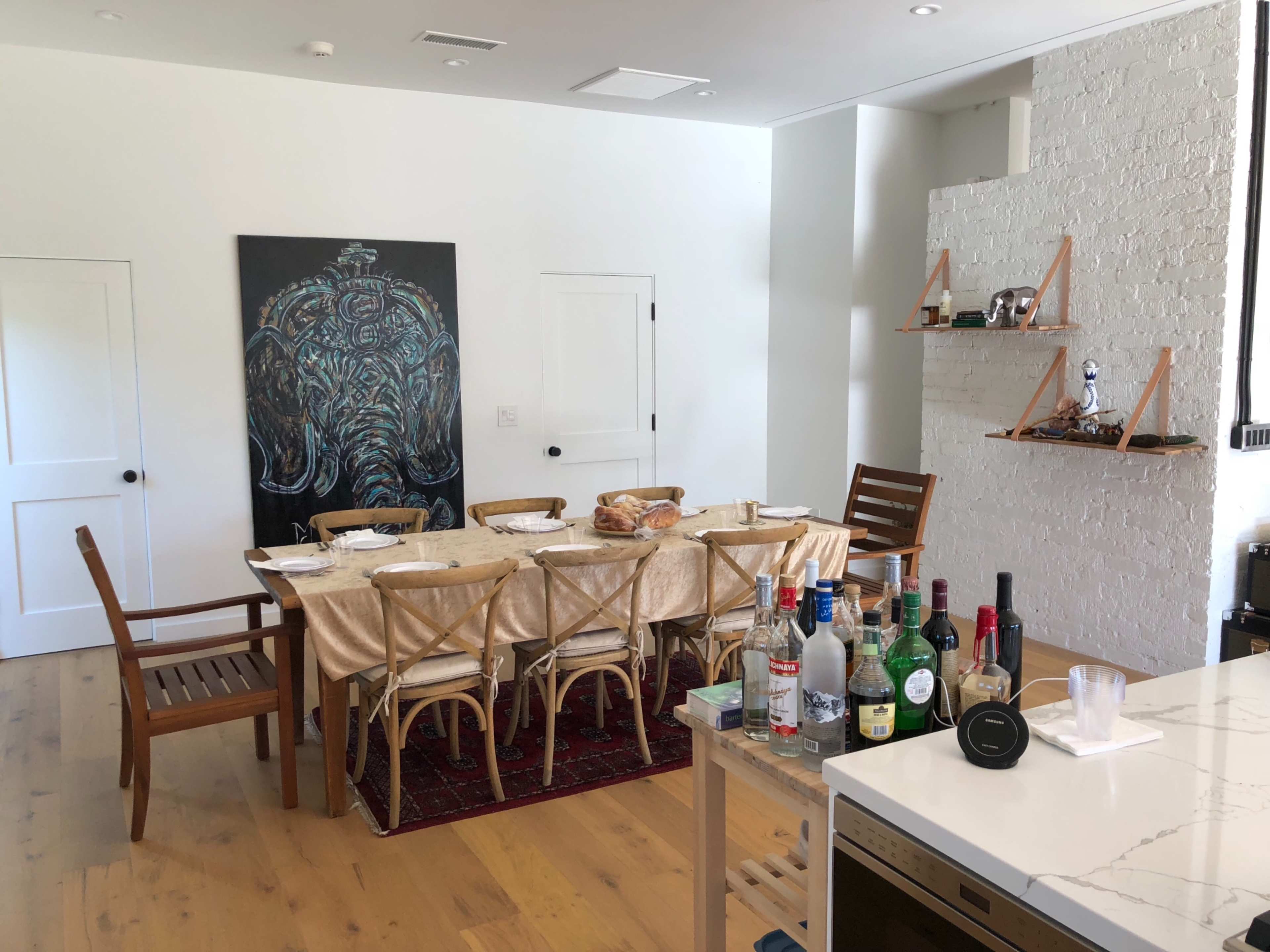 A dining room with a long table set for dinner, an elephant painting on the wall, and a bar area featuring various bottles.