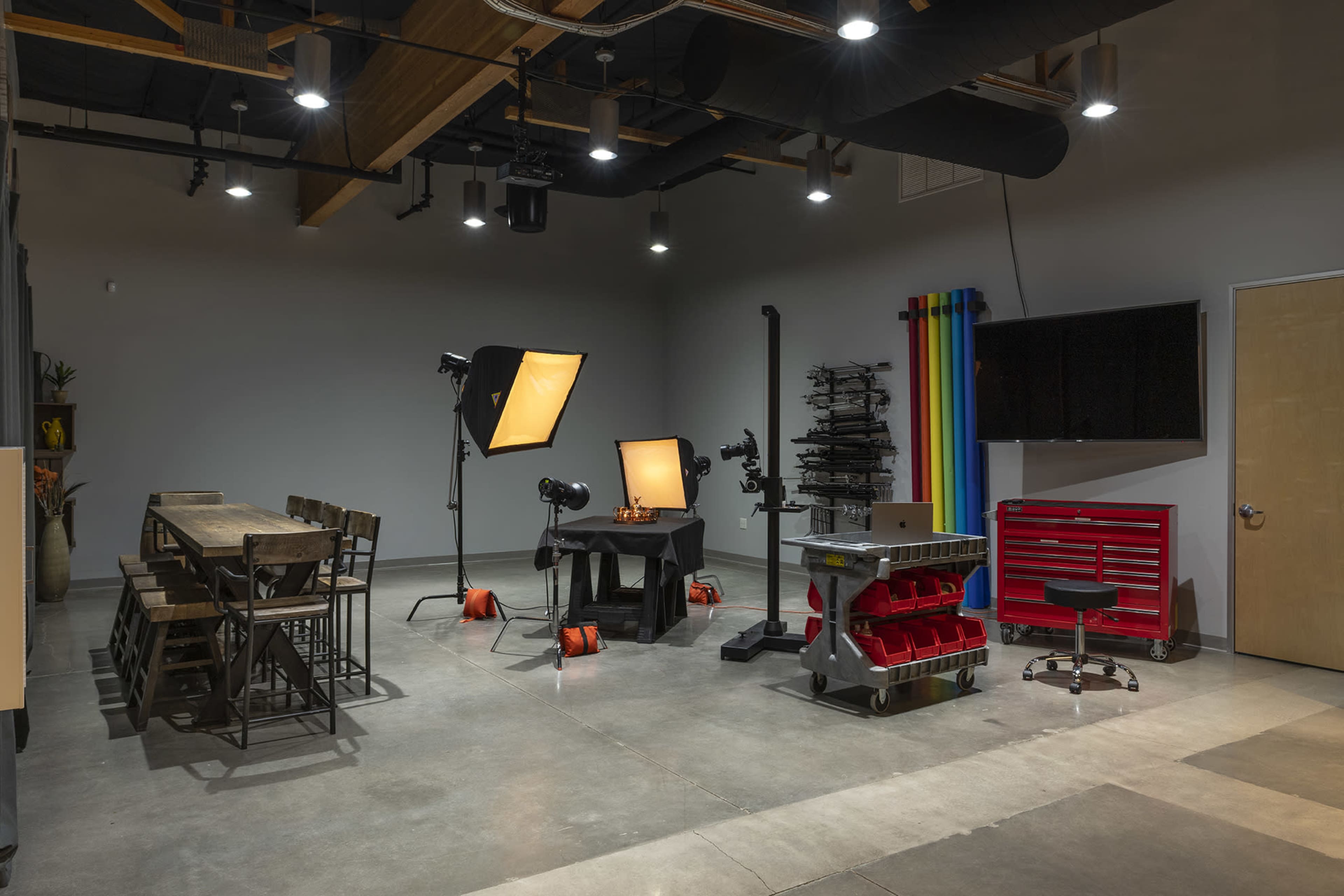 The image shows a photography studio equipped with lighting, a table, seating, and a workstation with tools.