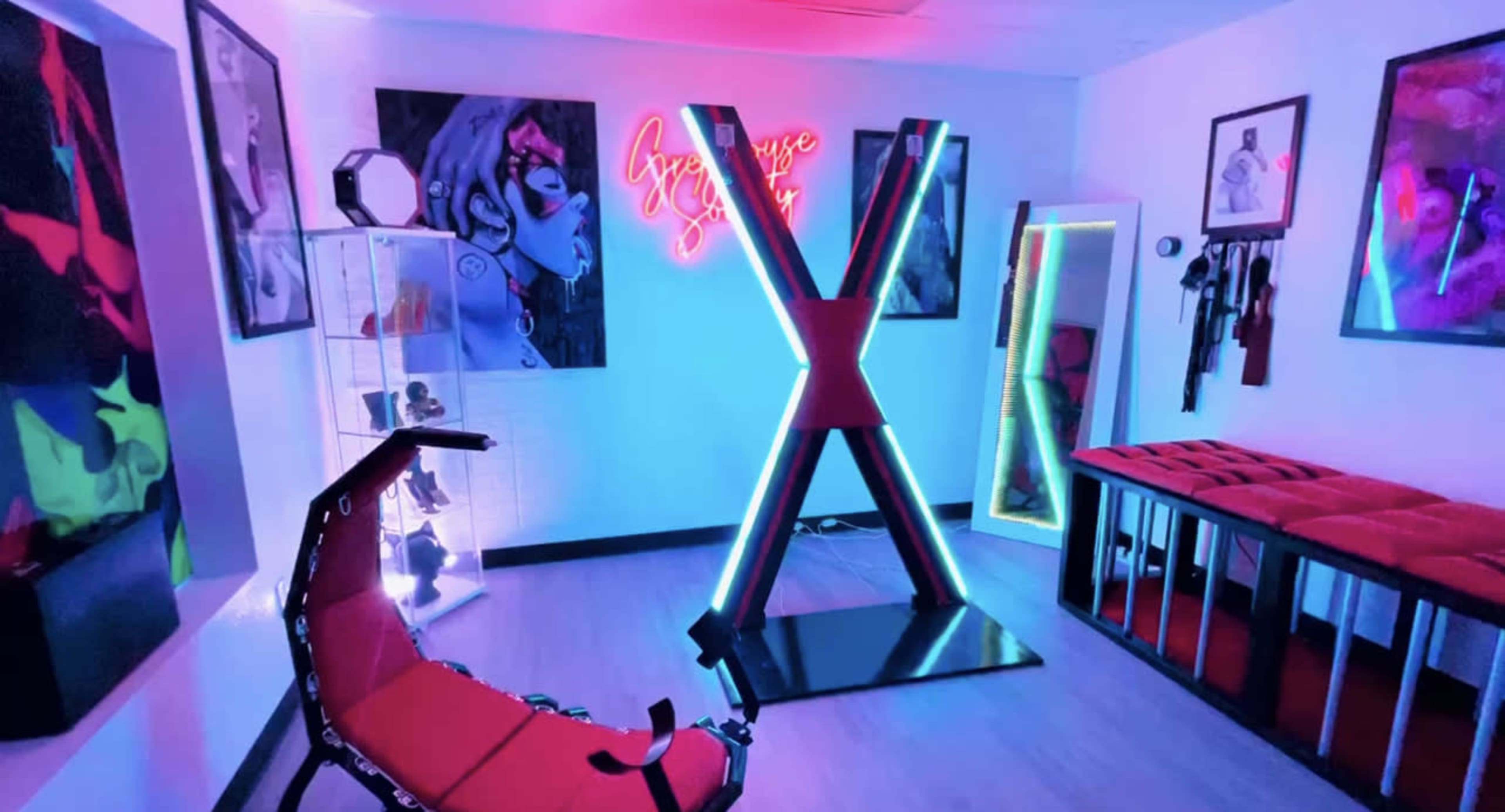 The room features vibrant neon lighting and modern furniture, including a red chair and a striking X-shaped display.