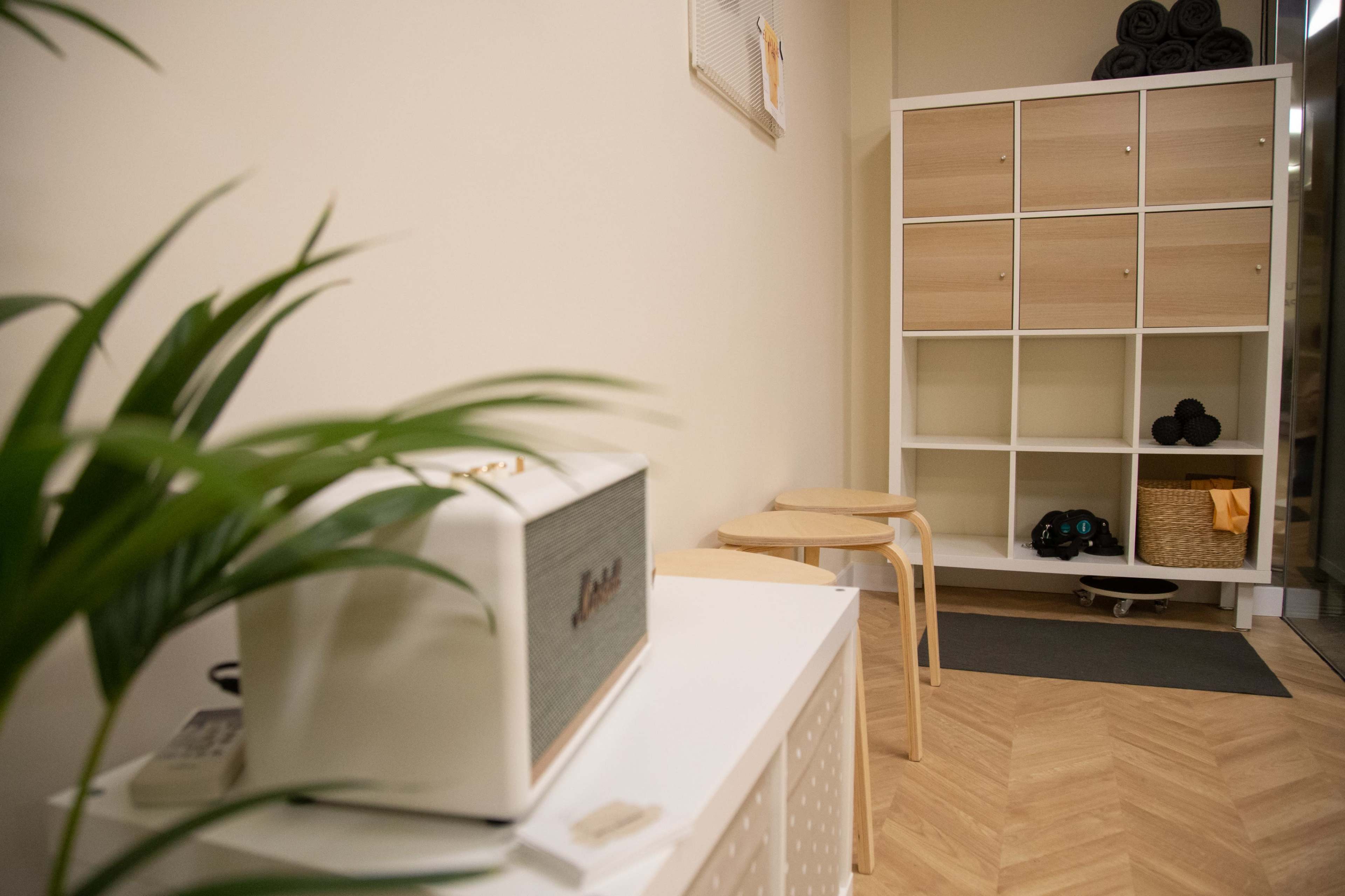 A minimalistic entryway features a white and wooden storage unit, stools, a plant, and a radio on a side table.
