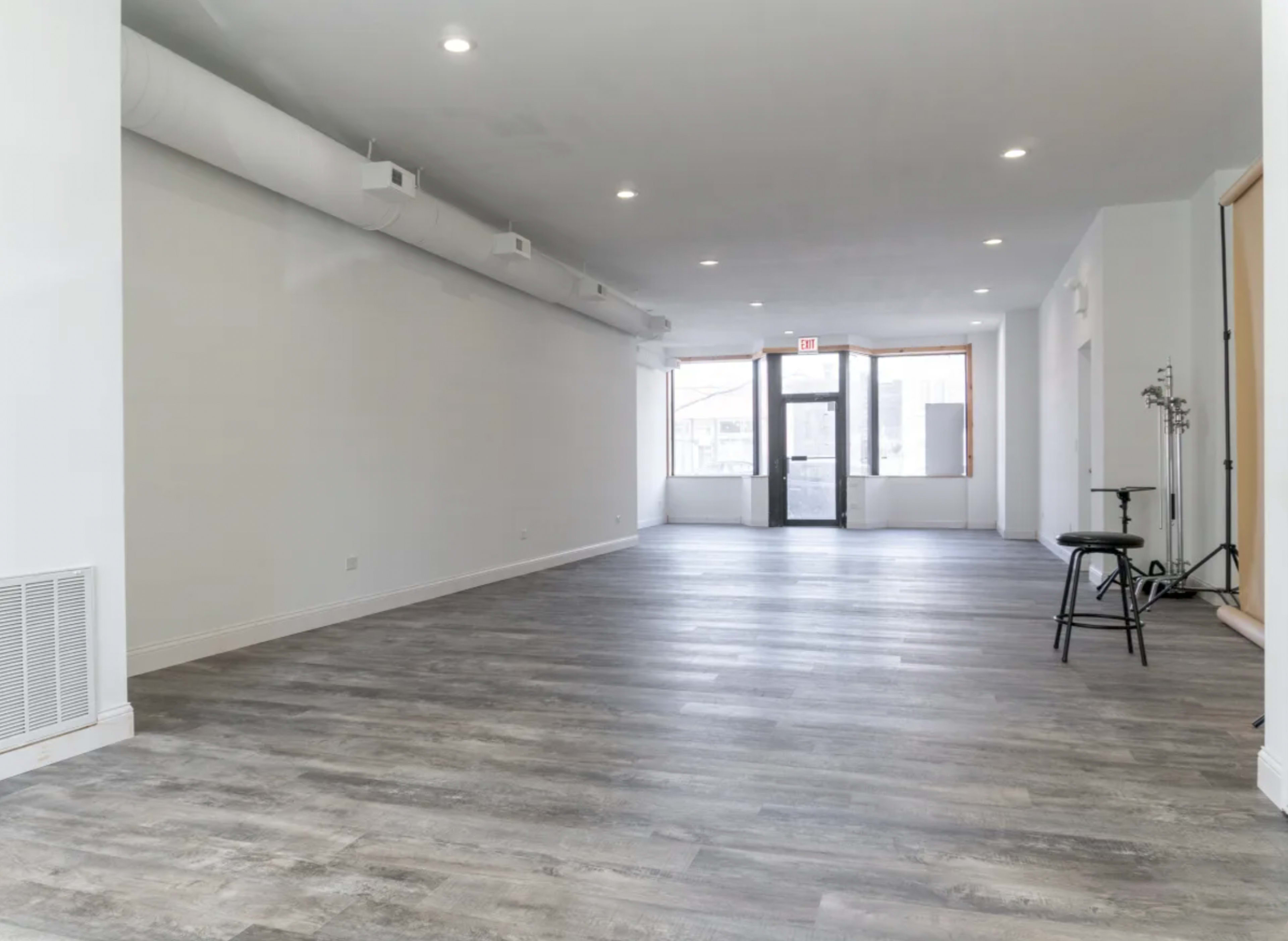 A large, empty room with wooden floors and a wide entrance door leading to the outside.
