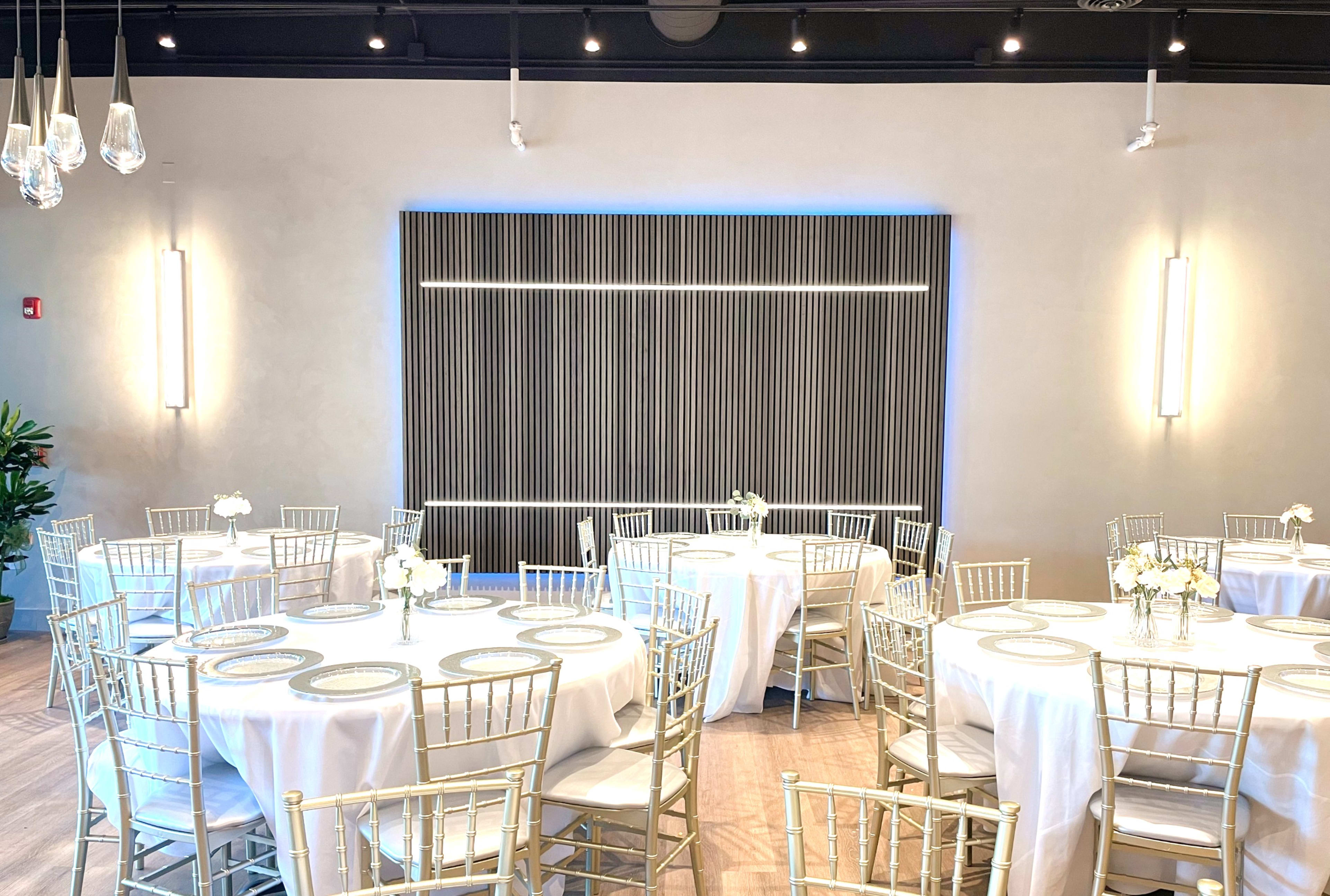 A banquet hall set with round tables, each dressed in white tablecloths and adorned with floral centerpieces, under modern lighting.