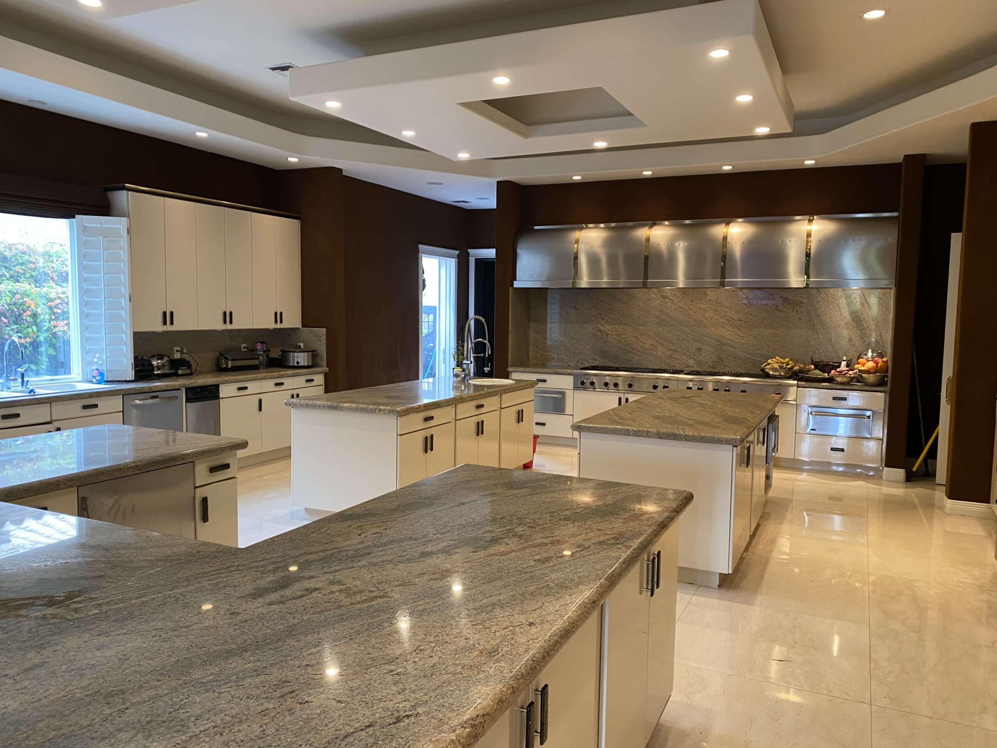 The image shows a spacious kitchen featuring multiple granite-topped islands, stainless steel appliances, and ample cabinetry.