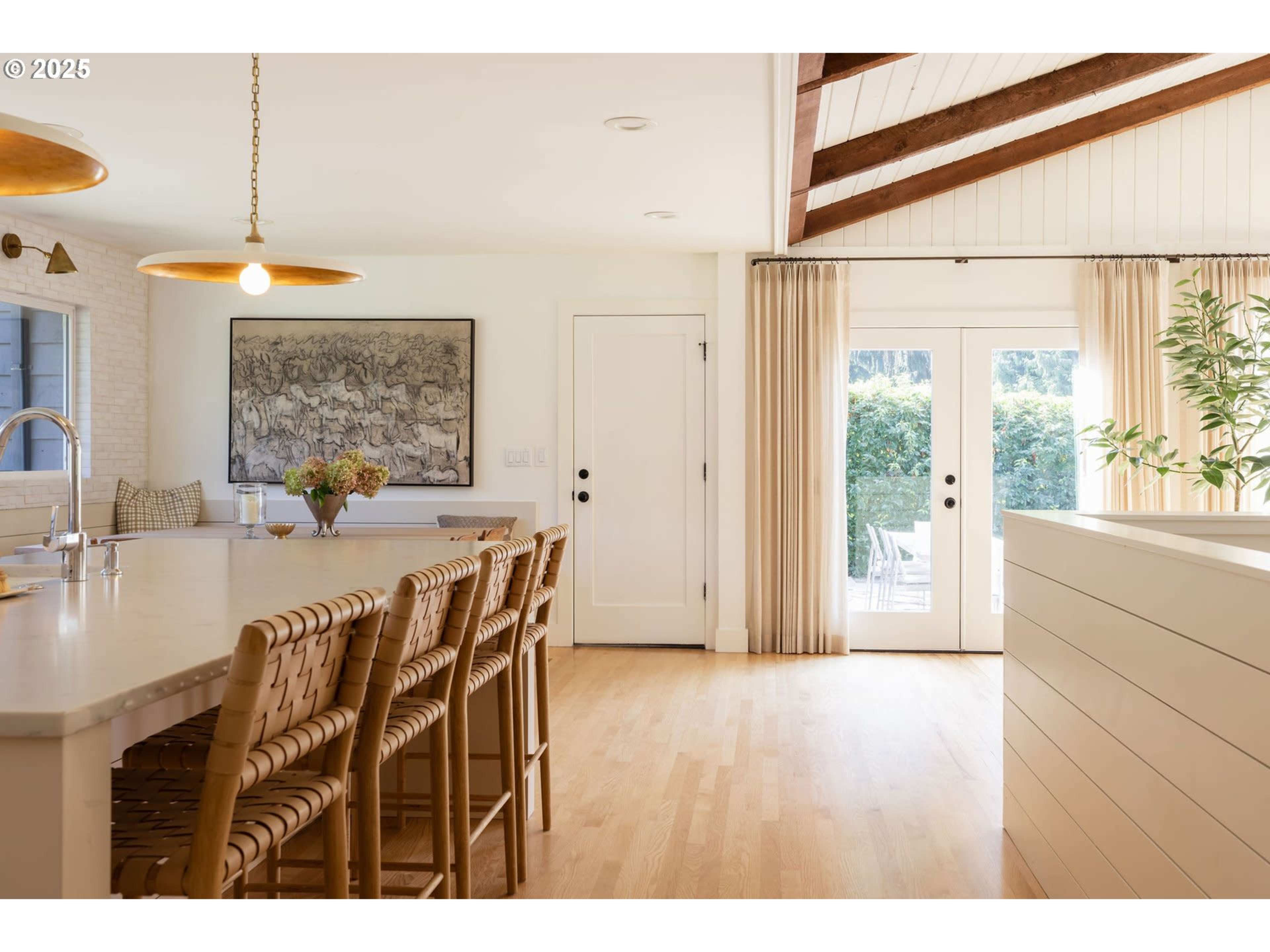 The image shows a bright kitchen featuring a large island with bar seating, a framed piece of art on the wall, and glass doors leading to an outdoor area.