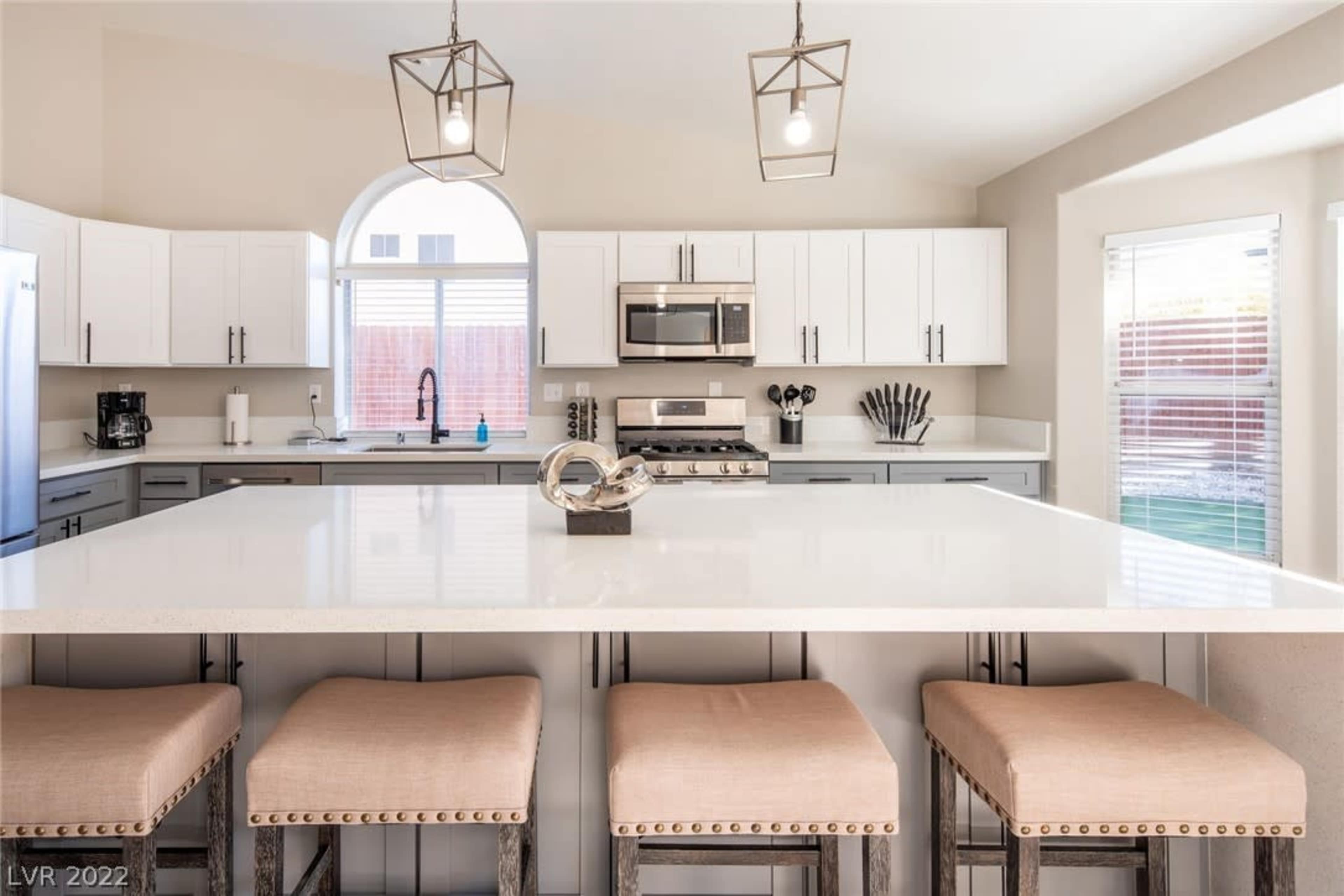 A modern kitchen features white cabinetry, stainless steel appliances, and a large island with seating for four.