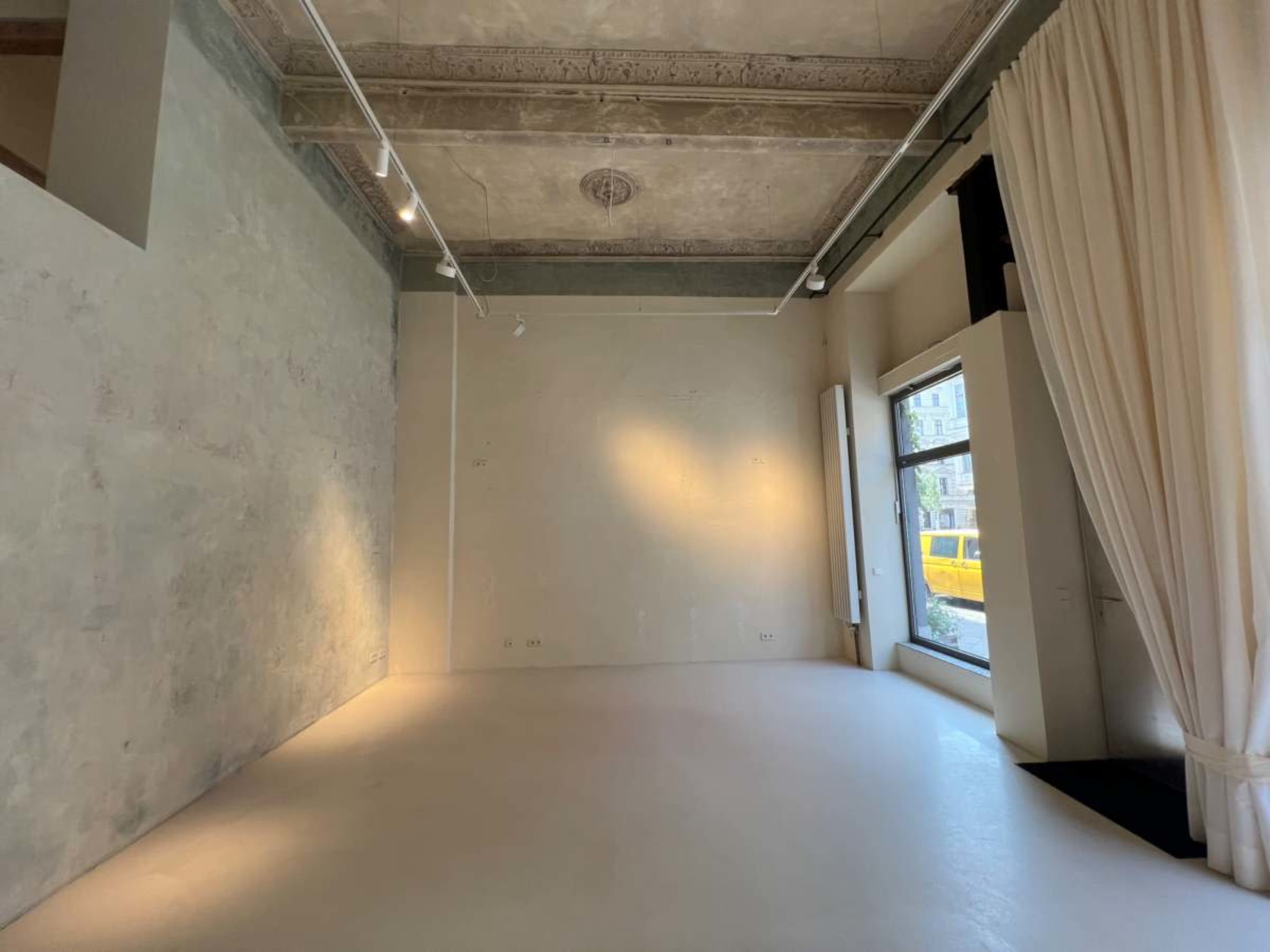 The image shows a sparsely furnished room with a textured wall, large window, and soft lighting.