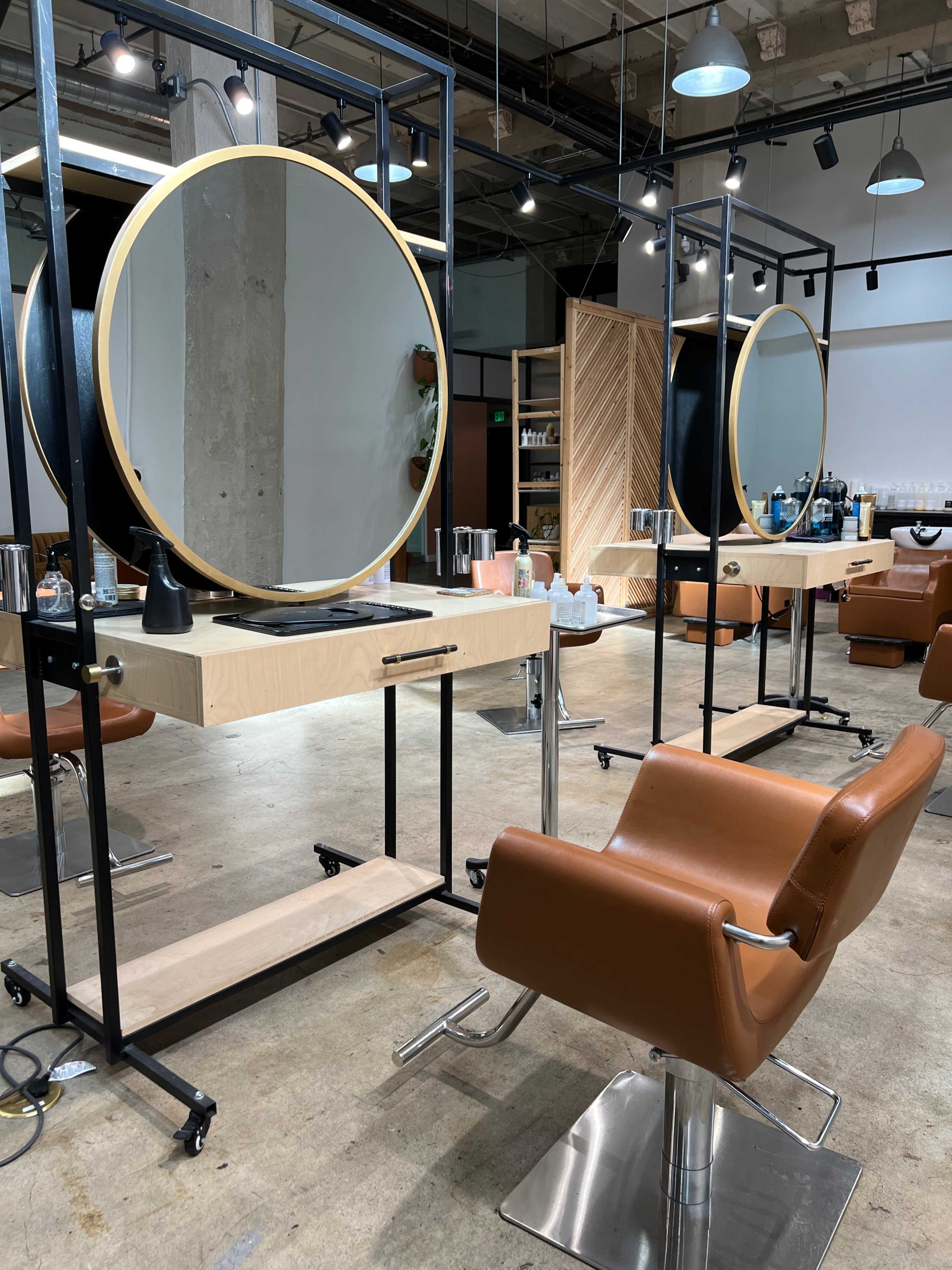 A modern hair salon with circular mirrors, wooden and metal styling stations, and leather chairs.