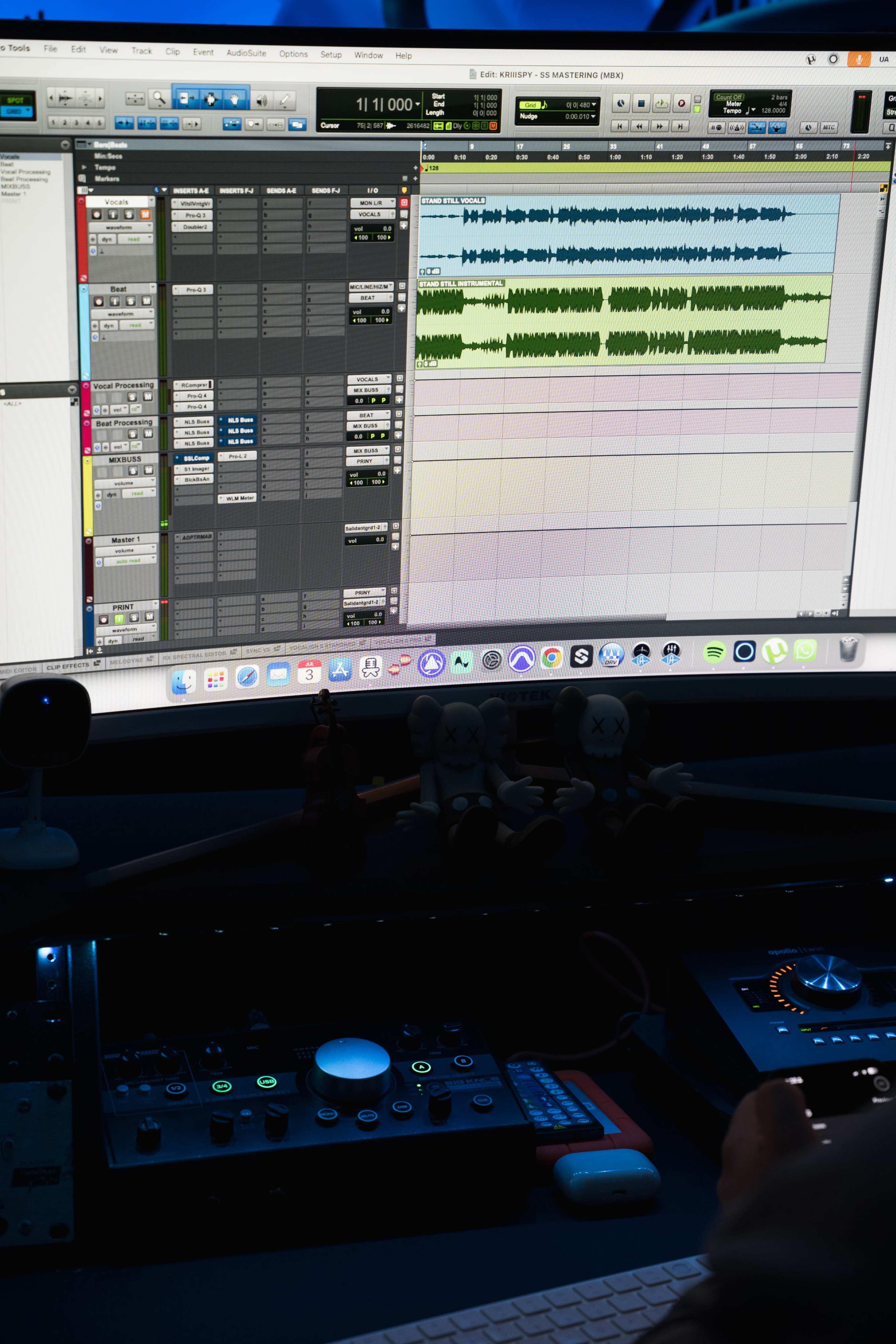 A close-up image of a computer monitor displaying audio editing software, with various audio tracks visible, while a hand adjusts a control knob on a nearby audio interface.