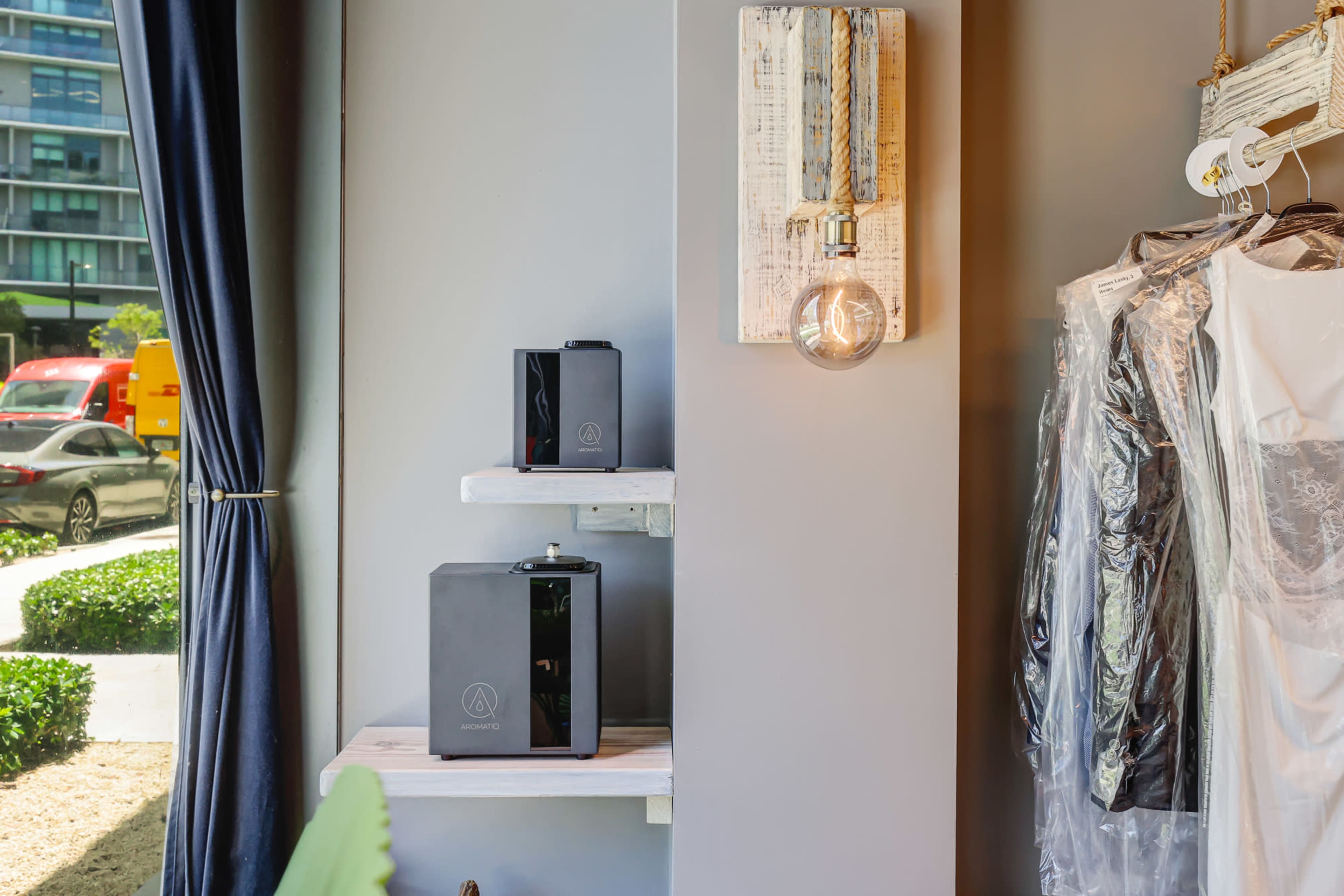 The image shows a retail space with two black speakers on shelves, a light bulb hanging from a wooden fixture, and clothing hung on a rack nearby.