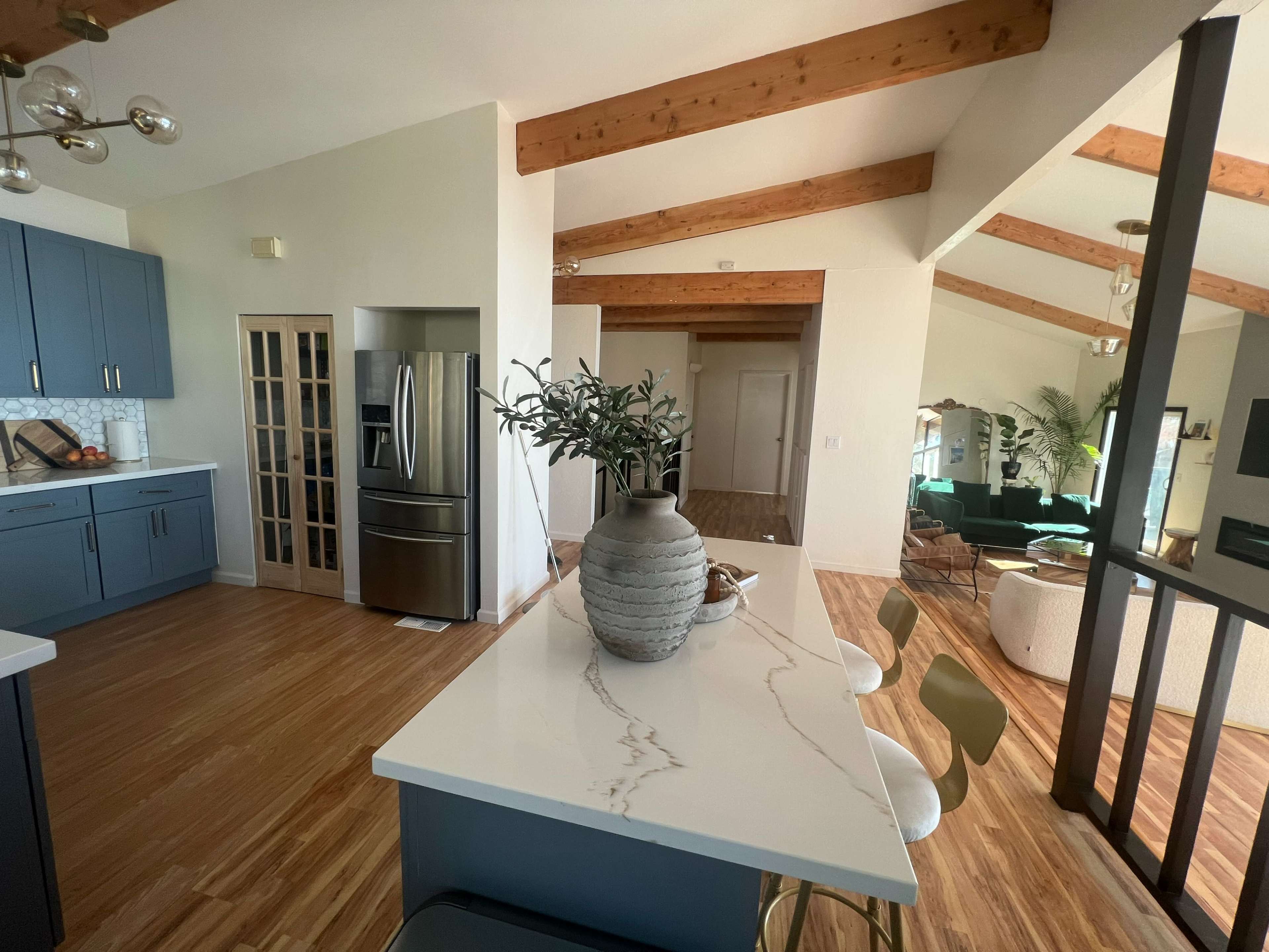 A modern kitchen features blue cabinetry and a marble countertop, leading into a living area with high ceilings and a mixture of furniture.