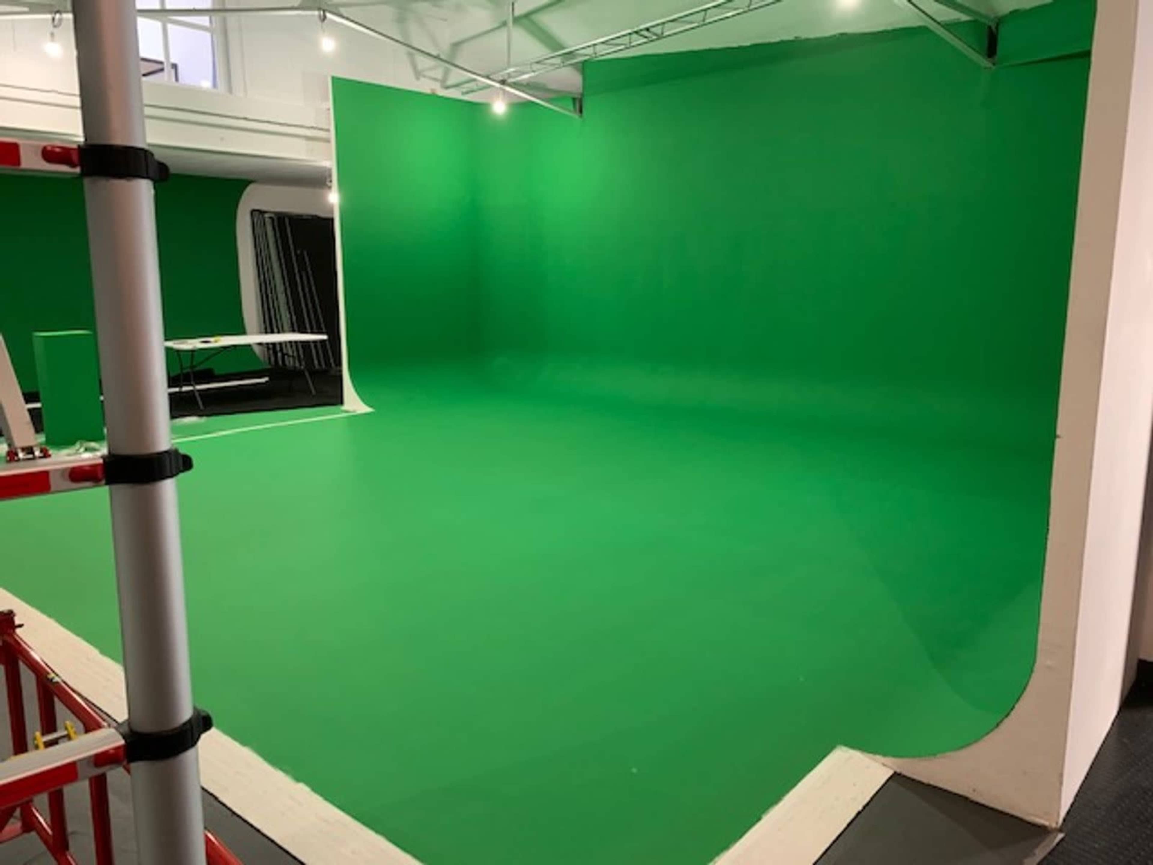 The image shows a green screen studio with a seamless green backdrop and tools for video production.