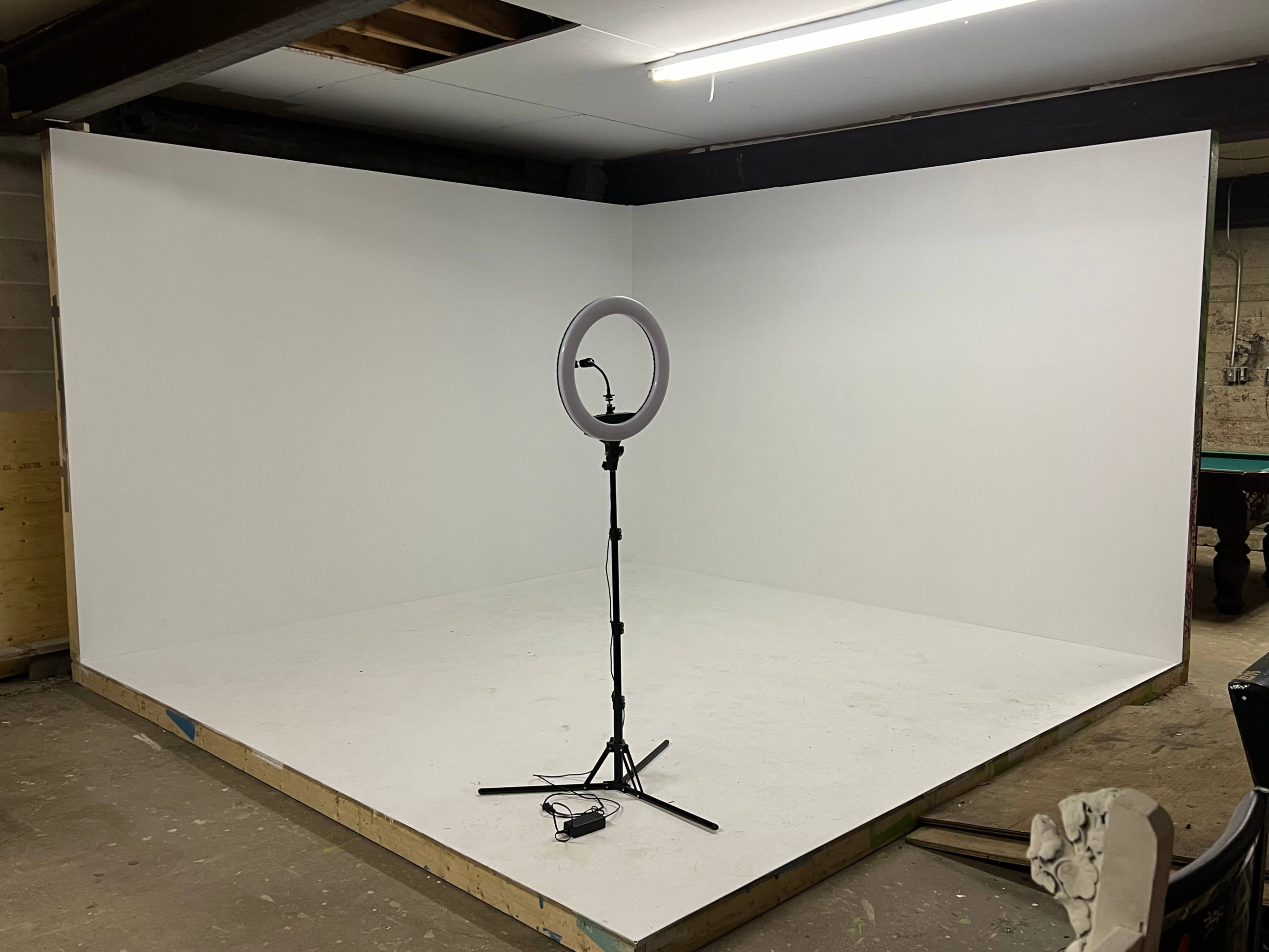 A plain, empty room with white walls and a ring light on a stand in the center.