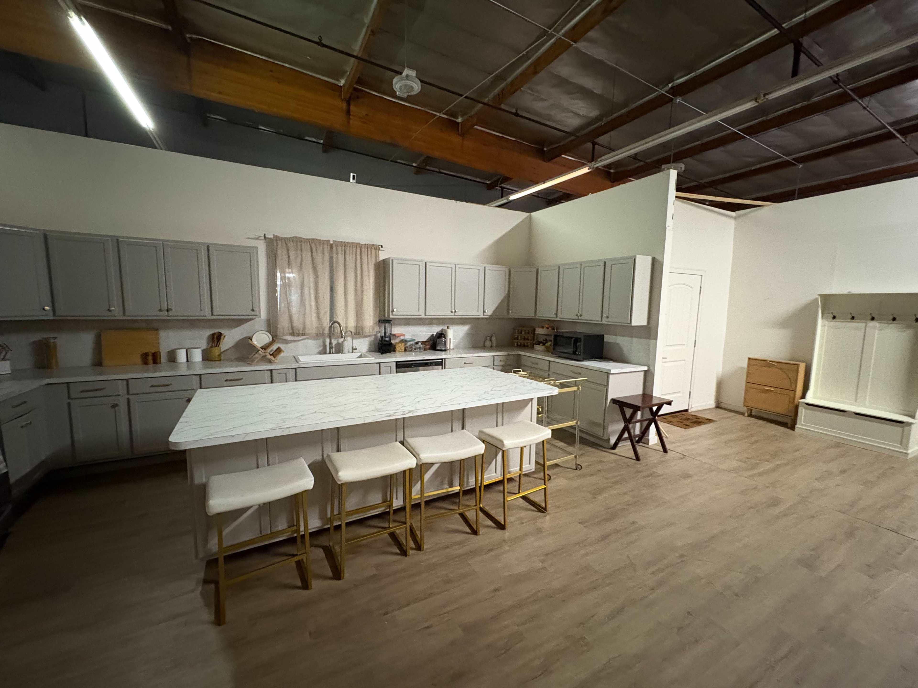 The image depicts a spacious kitchen with gray cabinets, a large white island with four stools, and natural light streaming through a window.