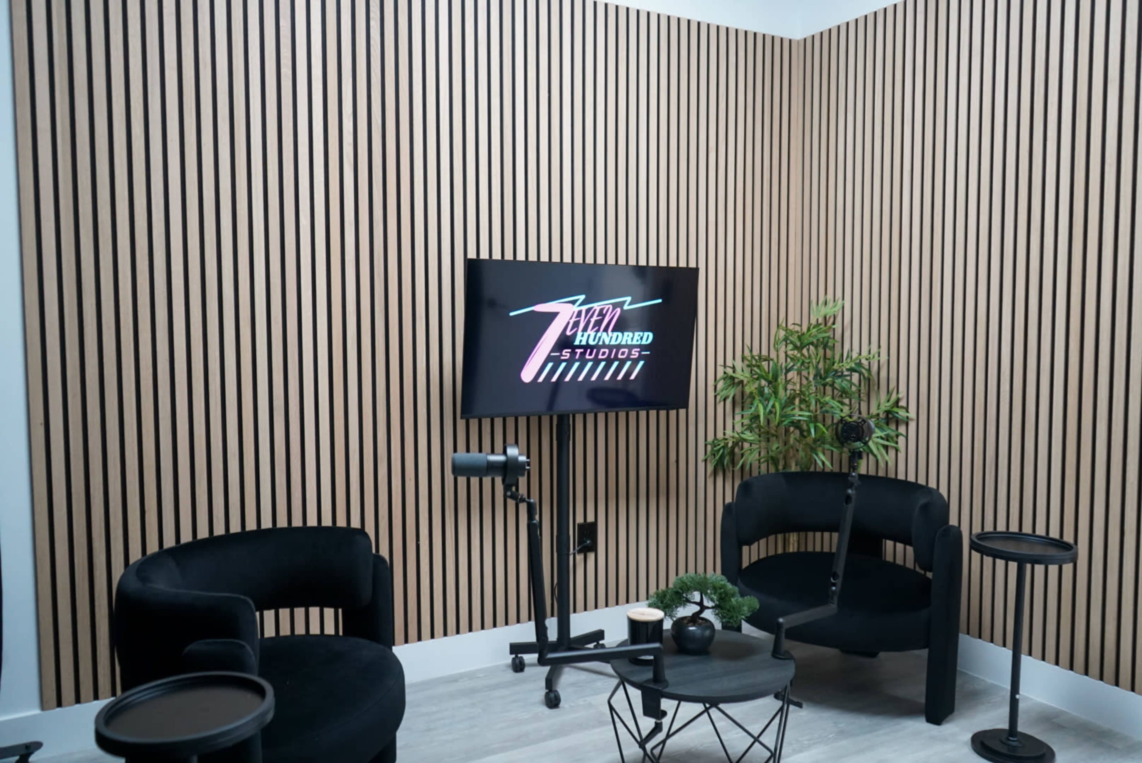 The image features a modern studio space with wooden slat walls, two black chairs, and a television displaying a logo for "Seven Hundred Studios."