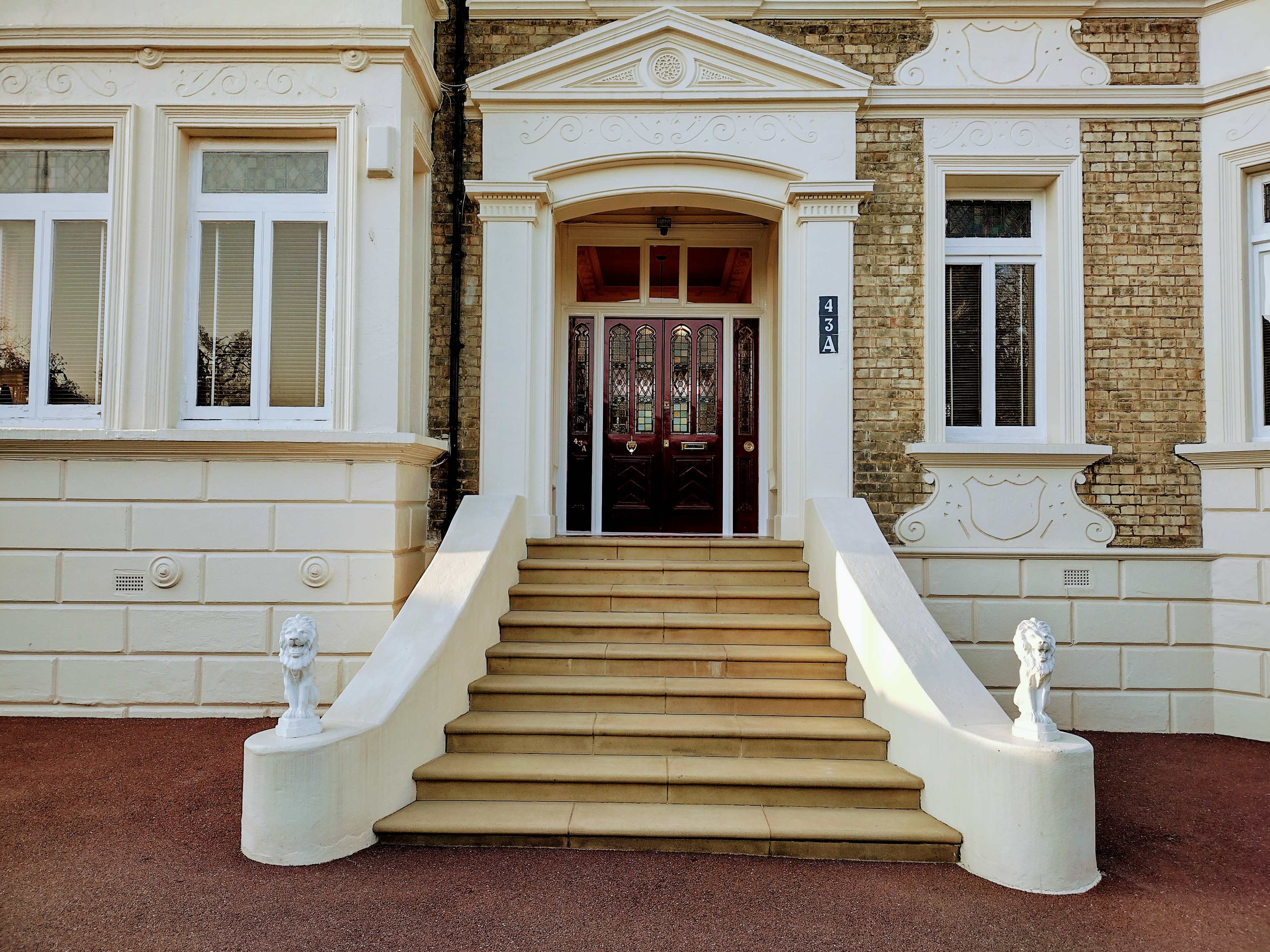 A building entrance with a set of steps leading up to double wooden doors, flanked by stone lion statues.
