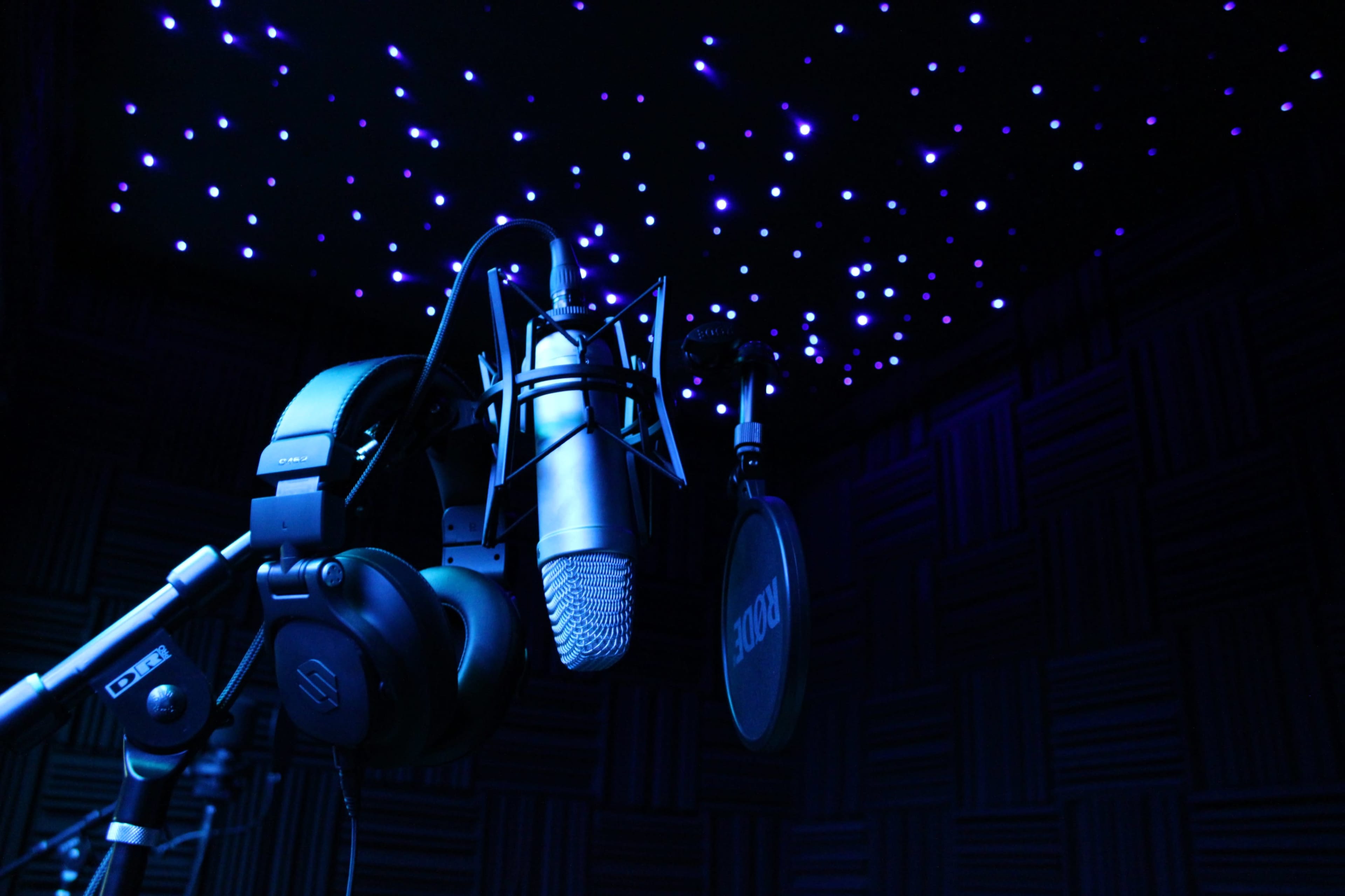 A microphone and headphones are positioned against a backdrop of a starry, illuminated ceiling in a sound studio.
