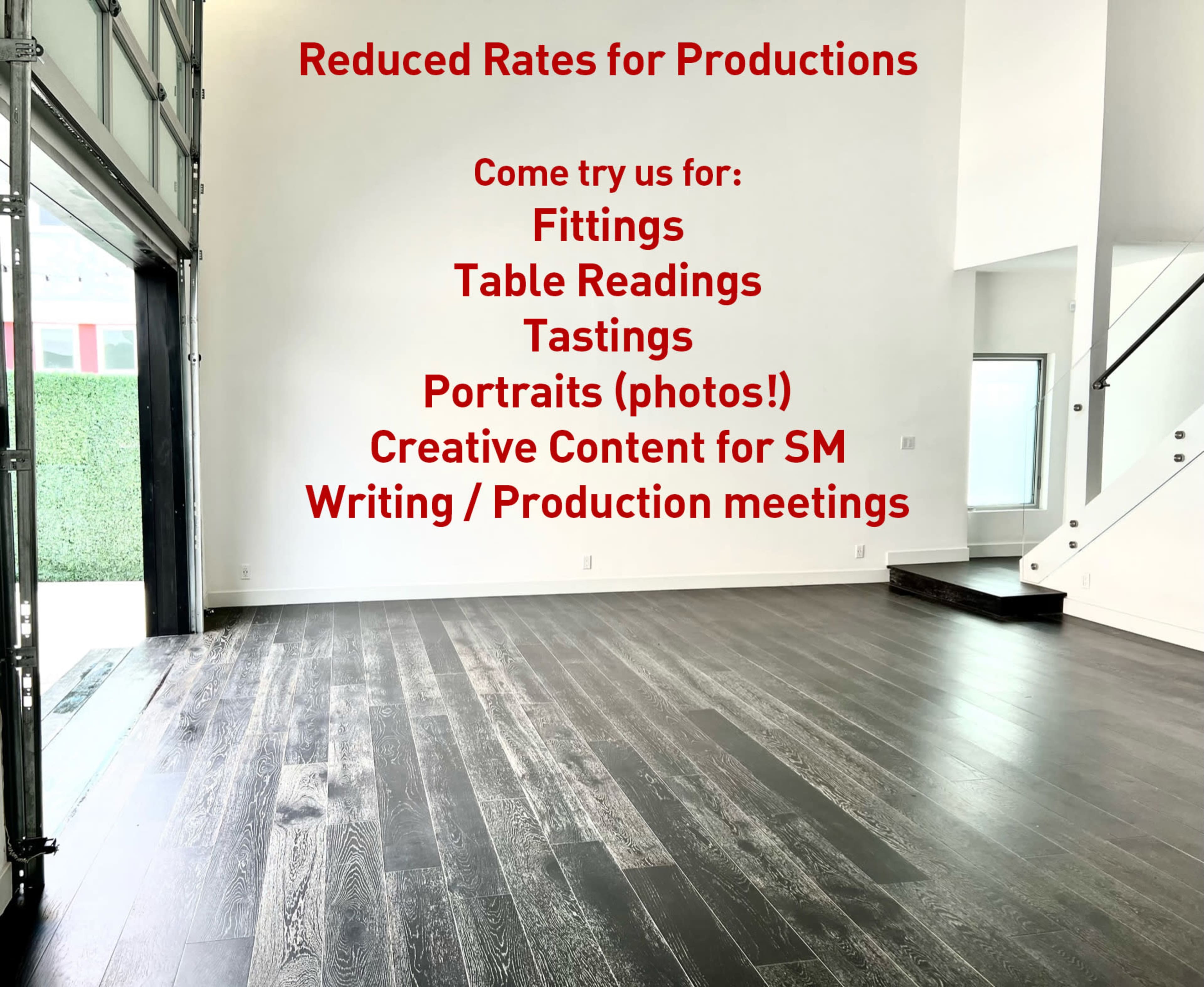 A spacious, empty room with hardwood flooring and a large wall featuring red text advertising reduced rates for various production services.