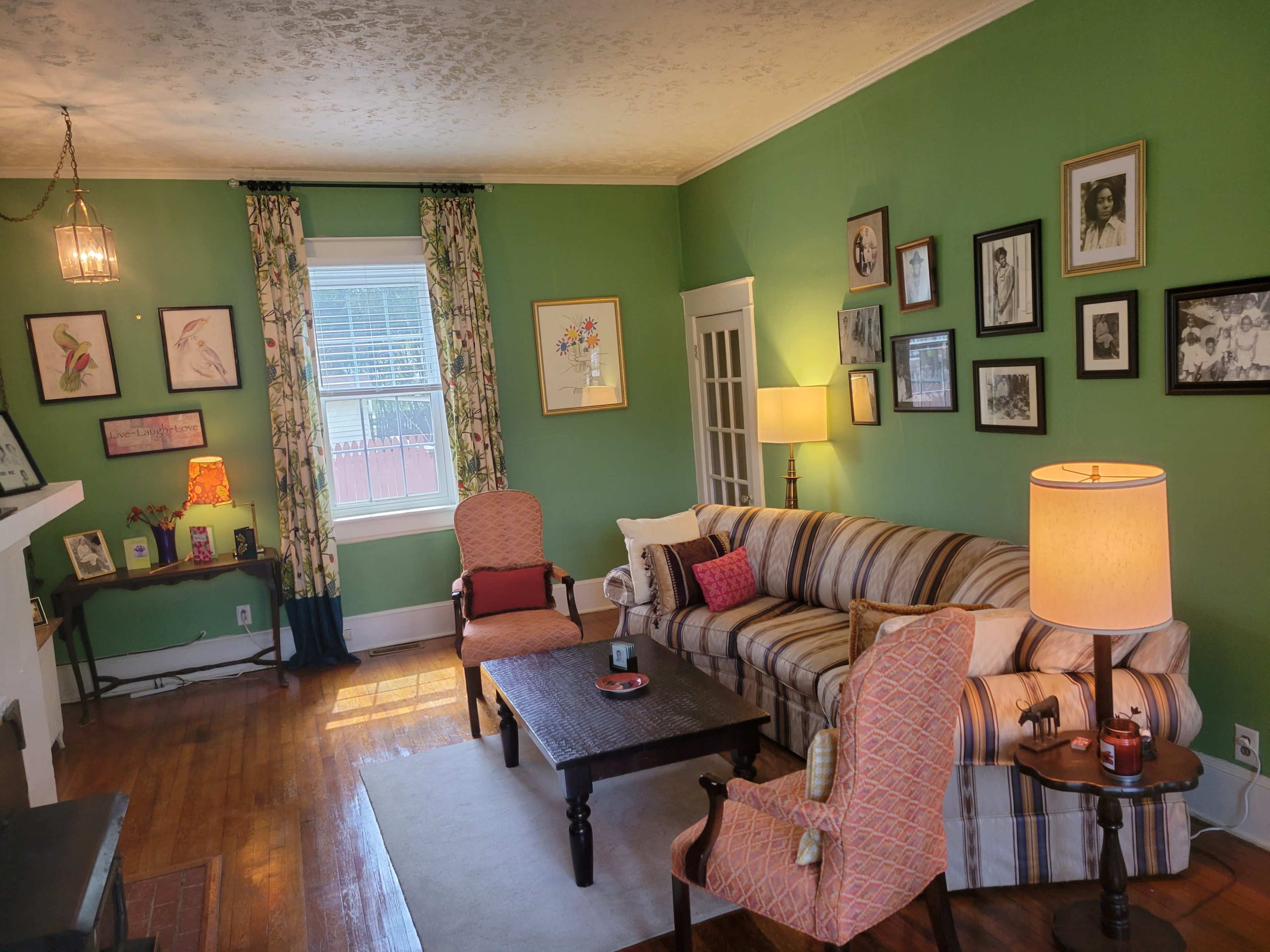 The living room features a green wall, a striped sofa, two armchairs, a coffee table, and various framed pictures hanging on the walls.