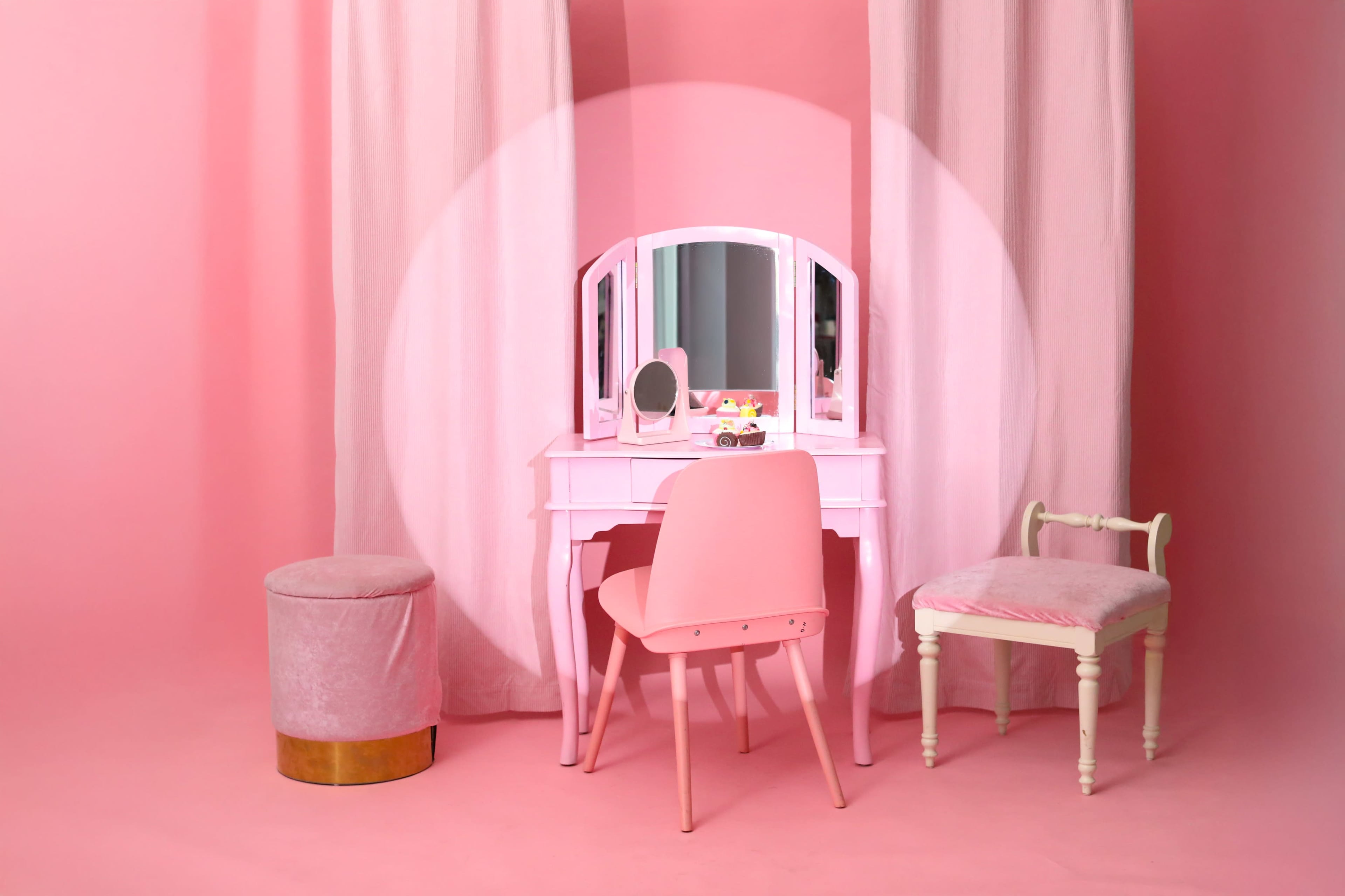 The image features a pink-themed vanity area, complete with a mirrored dressing table, two chairs, and a round stool.