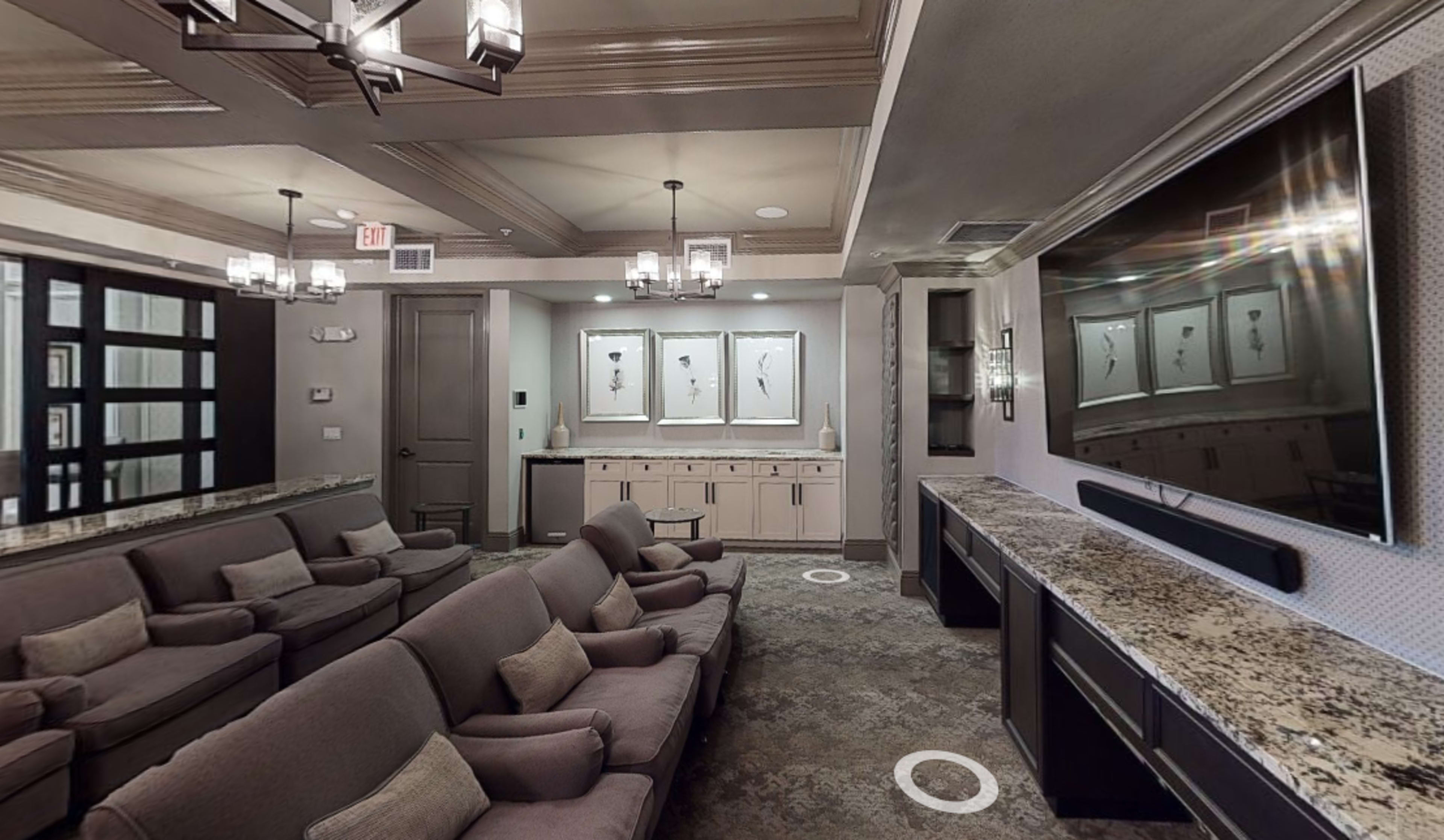 A modern home theater room with plush seating, a large television mounted on the wall, and decorative artwork displayed in a gallery.