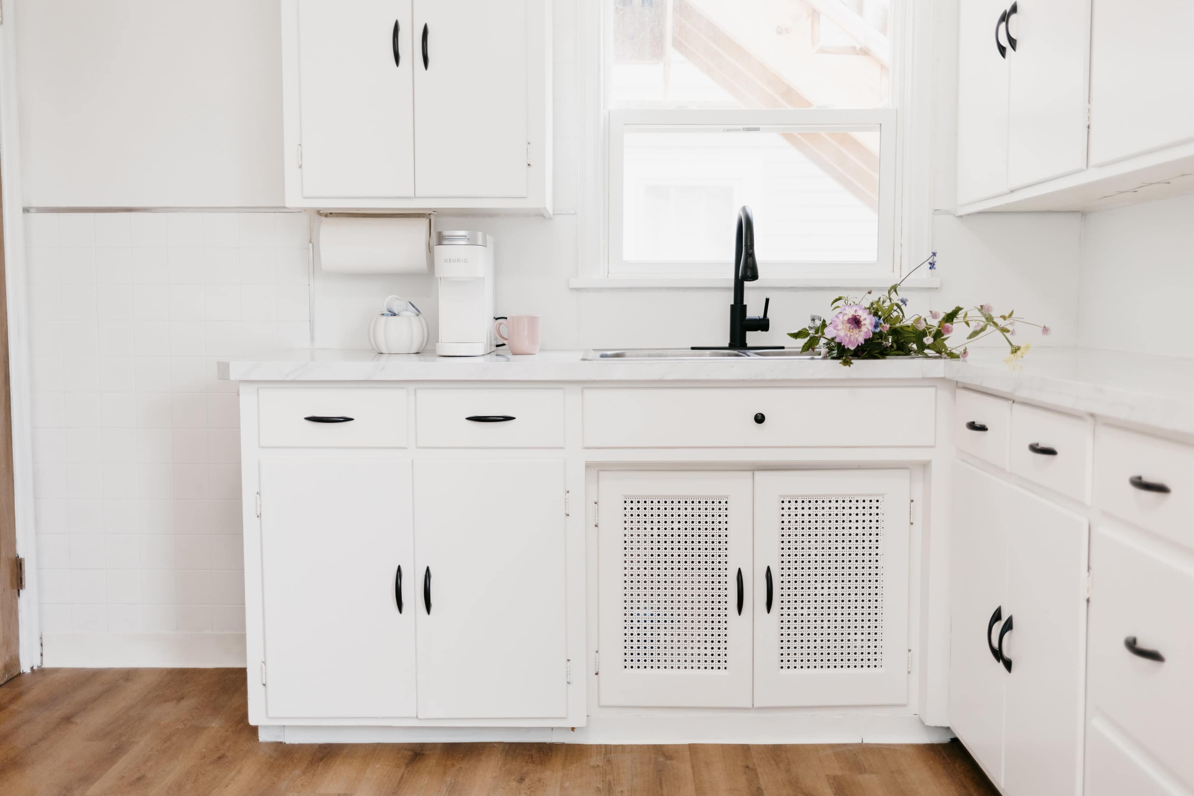 A minimalist kitchen features white cabinets, a sink with a black faucet, and a small vase of flowers on the countertop.