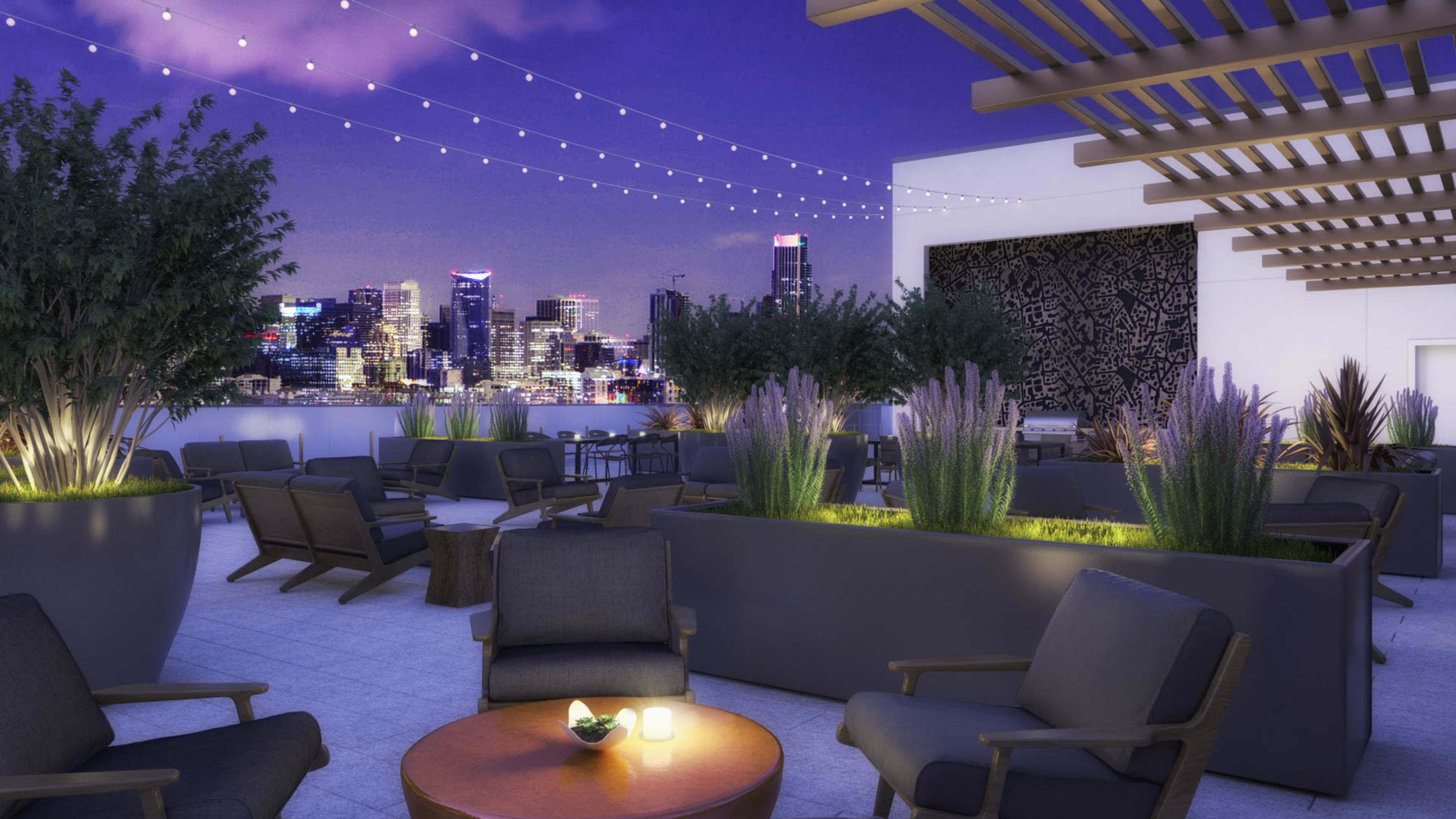 A rooftop terrace features comfortable seating, potted plants, and string lights, overlooking a city skyline at twilight.