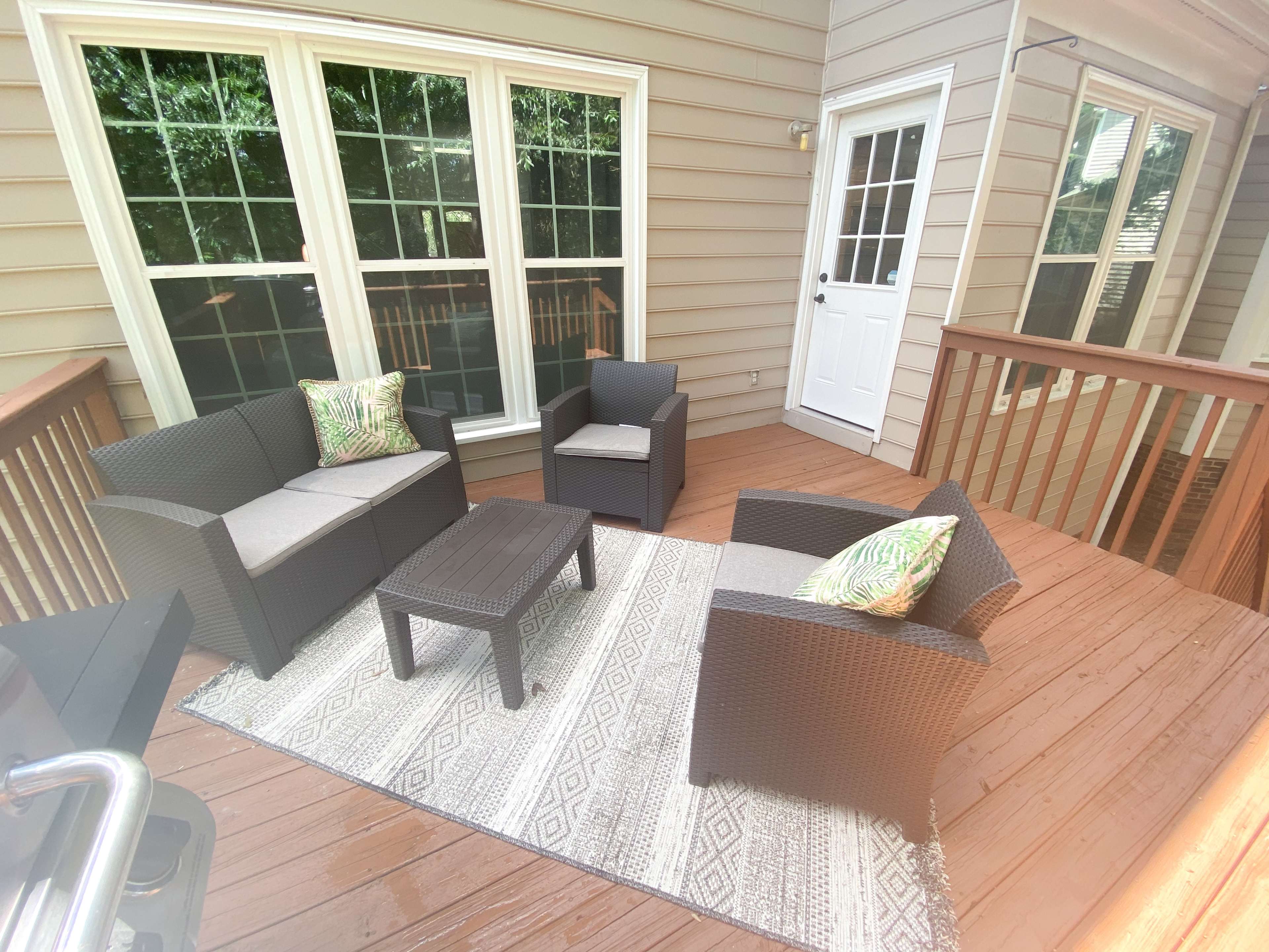 A patio features a seating arrangement with wicker furniture and a patterned rug, alongside a door leading outside.