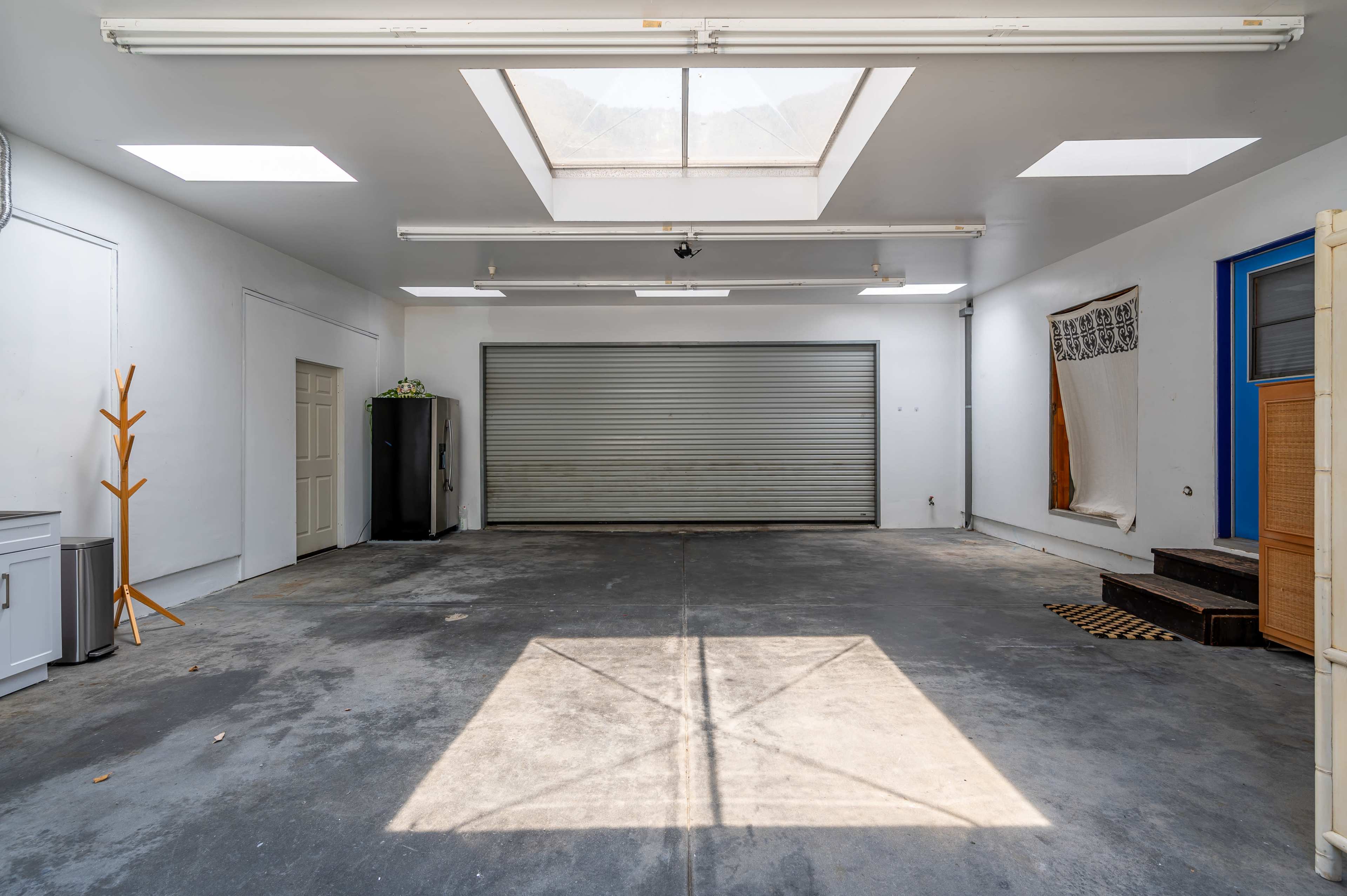 A spacious, empty garage with a large overhead skylight and a metal rolling door partially closed.