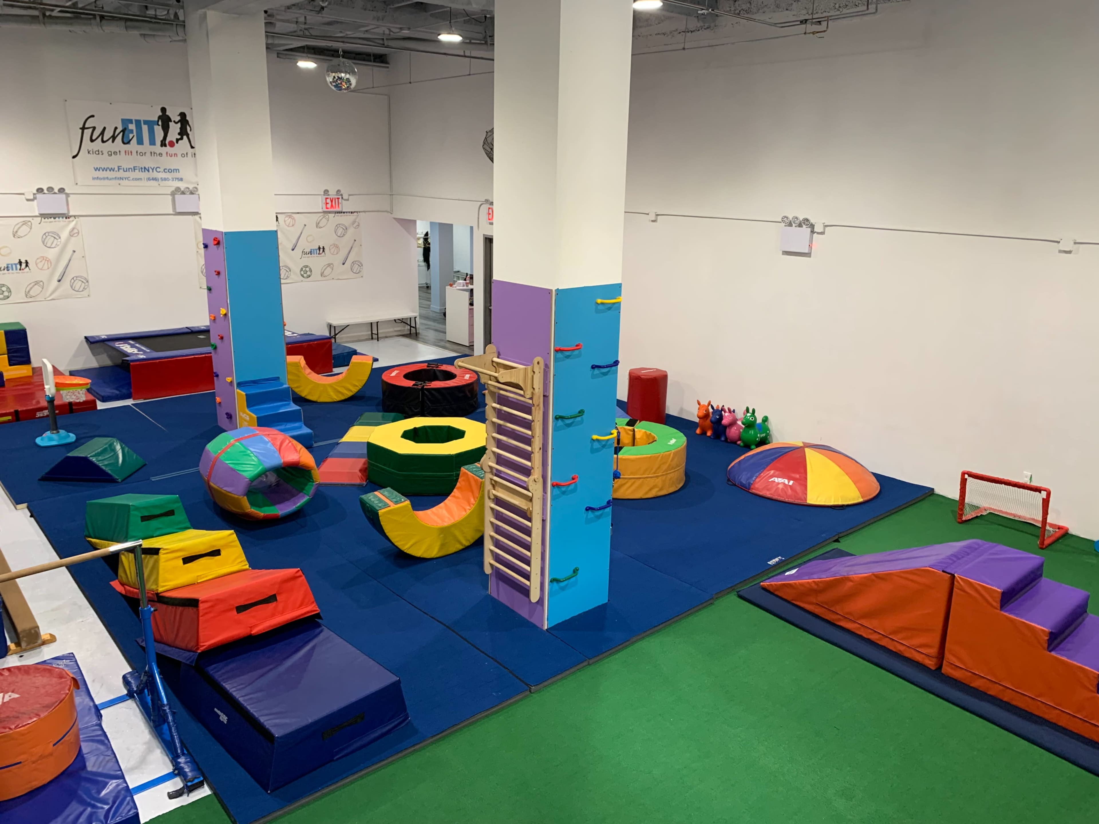 The image shows an indoor gymnasium designed for children's activities, featuring various colorful soft play equipment and mats arranged on the floor.