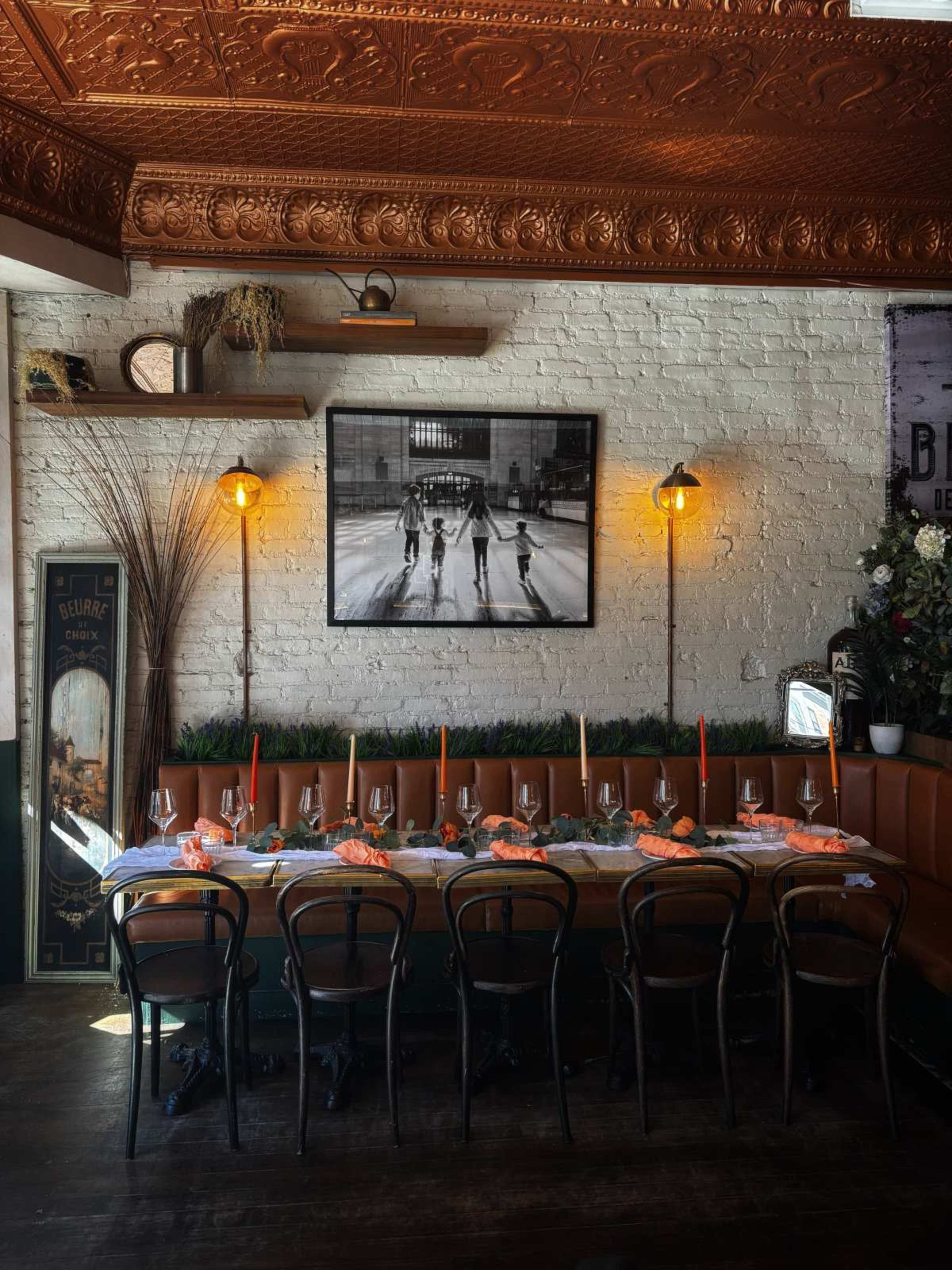 The image shows a dining setup with a long table adorned with orange napkins and candles, against a backdrop of brick walls and a large black-and-white photograph of basketball players.