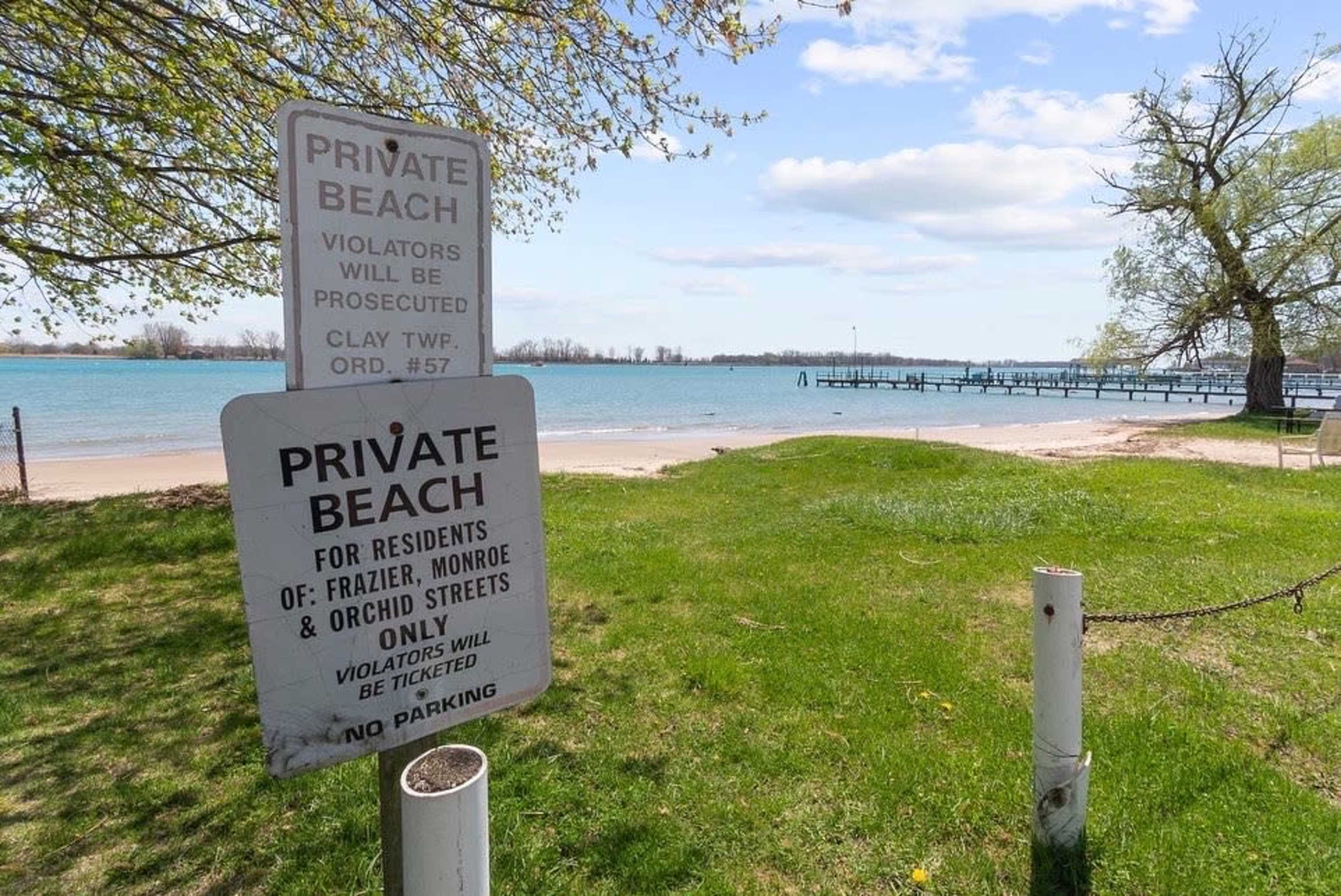 A sign indicating a private beach with restrictions located near a waterfront and a pier.