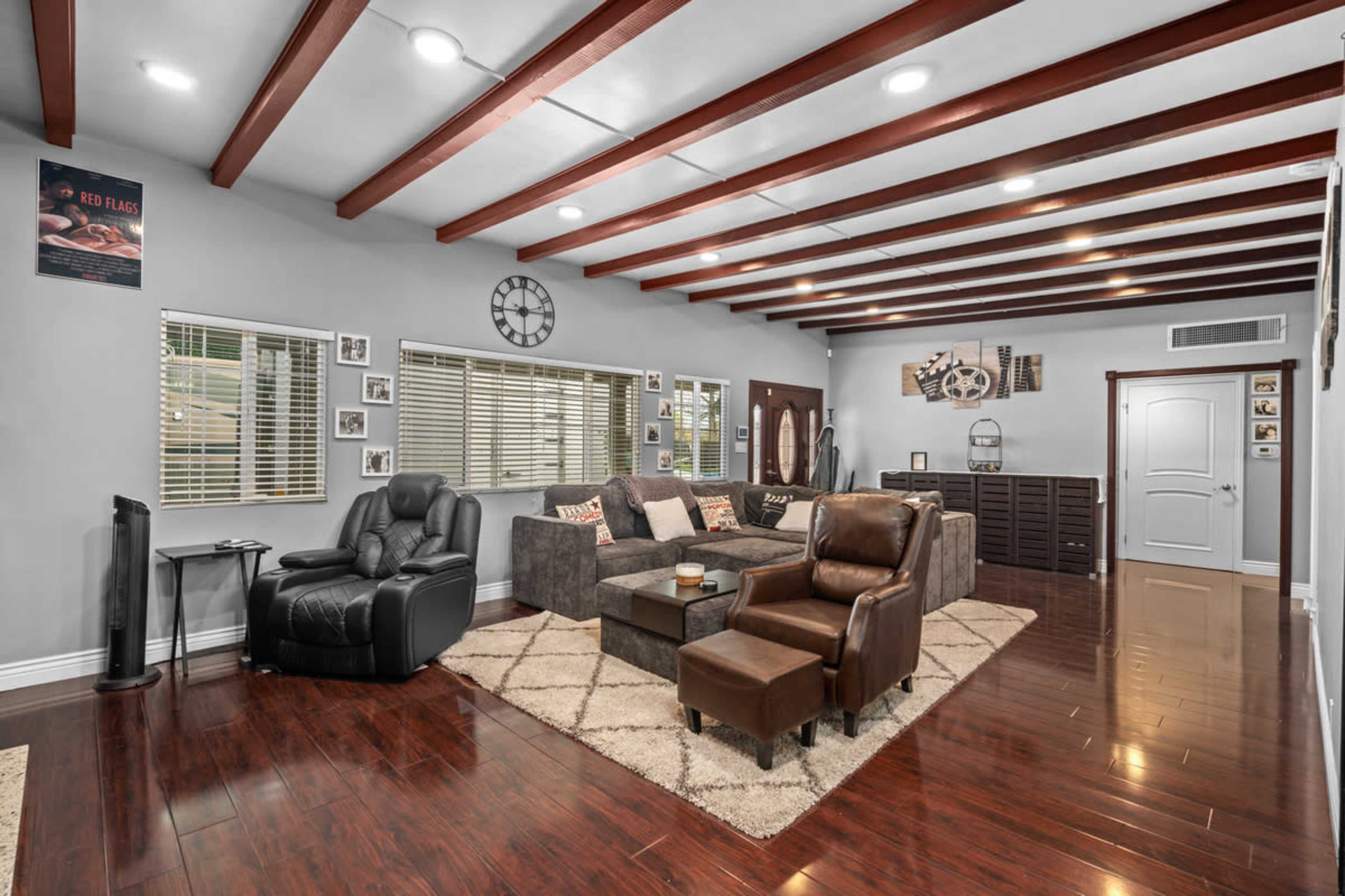 The living room features a sectional sofa, two armchairs, and a coffee table within a space highlighted by wooden beams on the ceiling and natural light from windows.