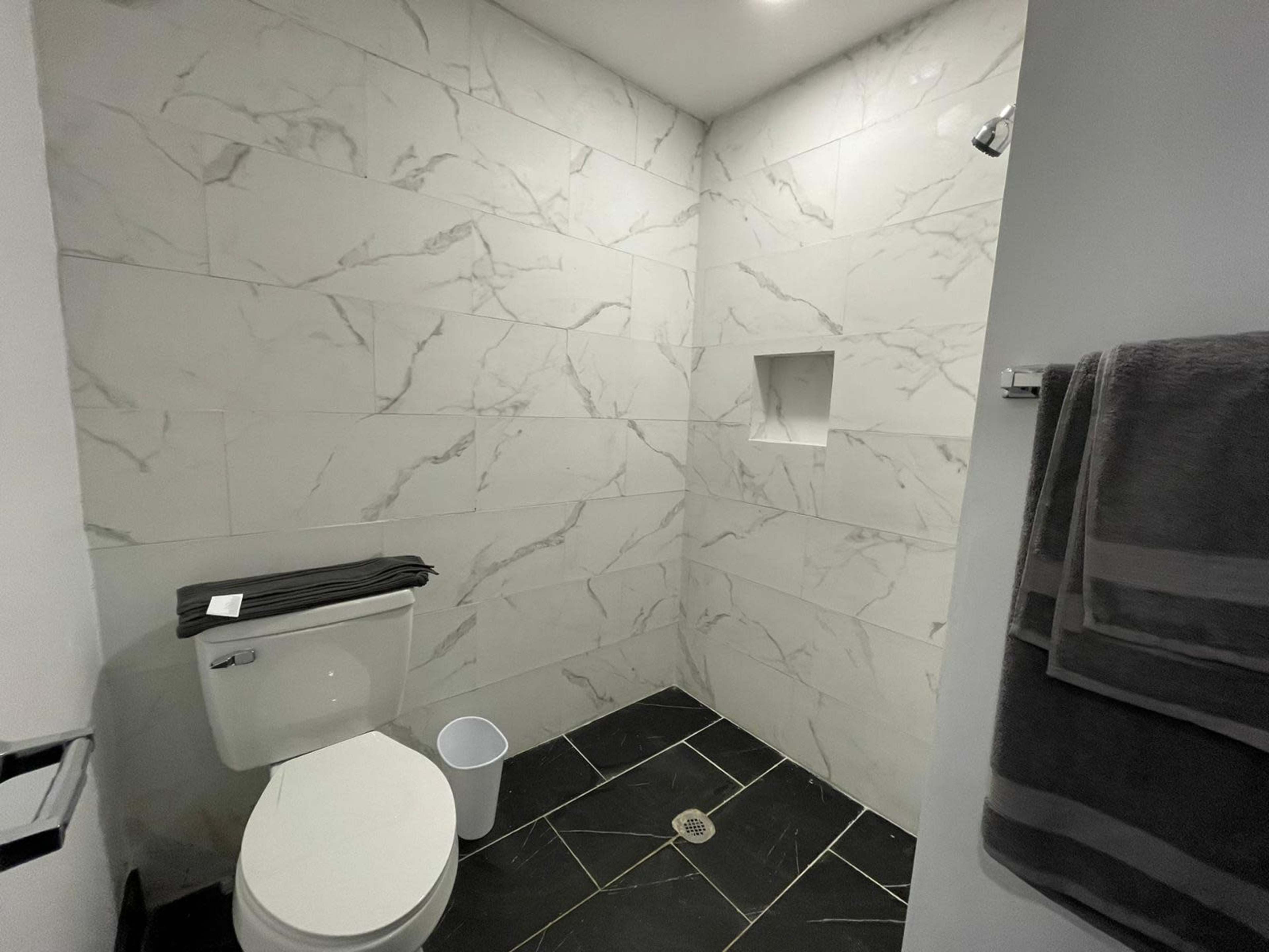 The image shows a bathroom with a tiled shower area, a toilet, and a towel rack.