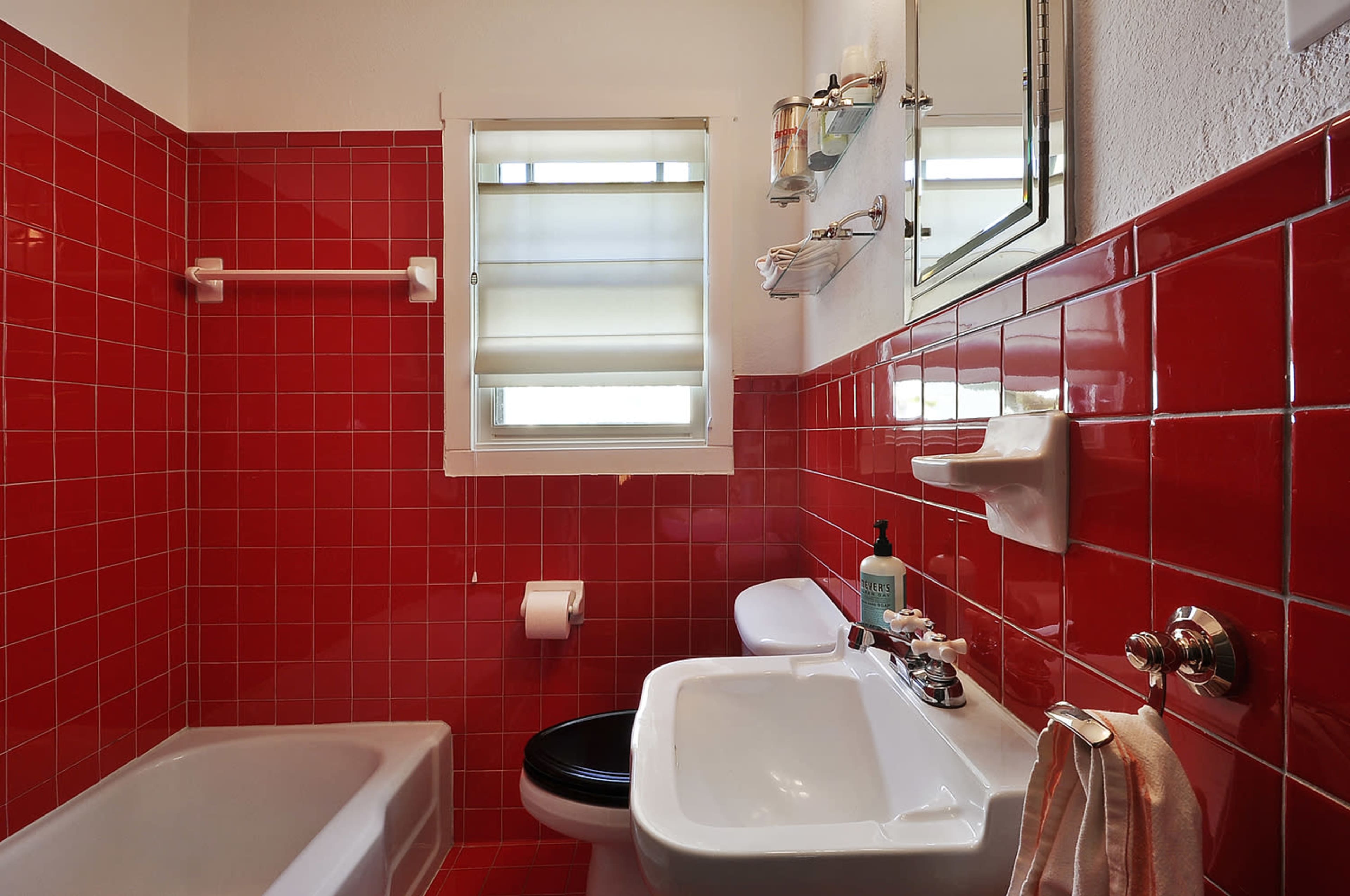 The bathroom features red tiled walls, a bathtub, a white sink, and a window with blinds.
