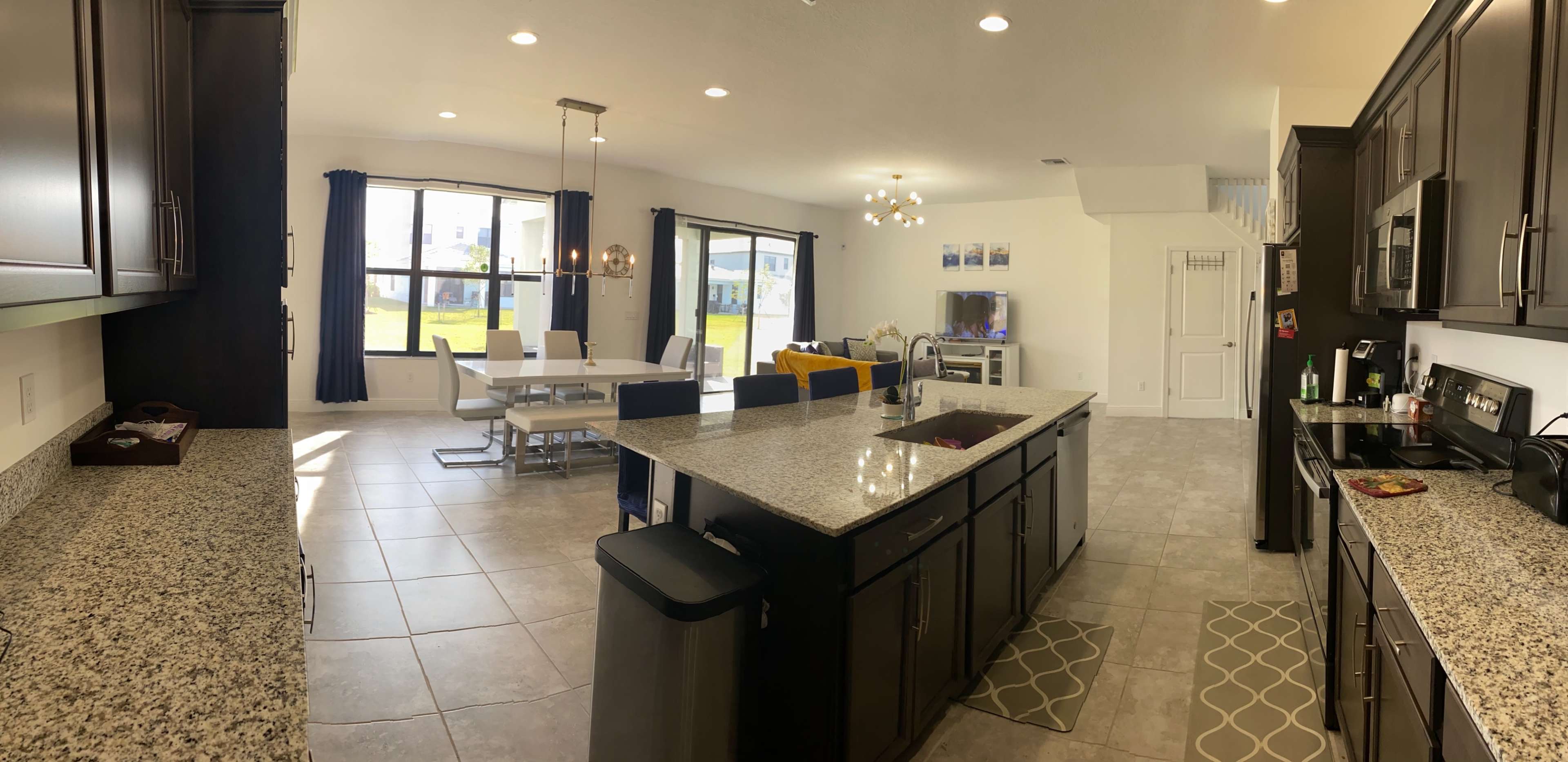 A modern kitchen with granite countertops opens to a dining area and living room, featuring large windows that provide natural light.