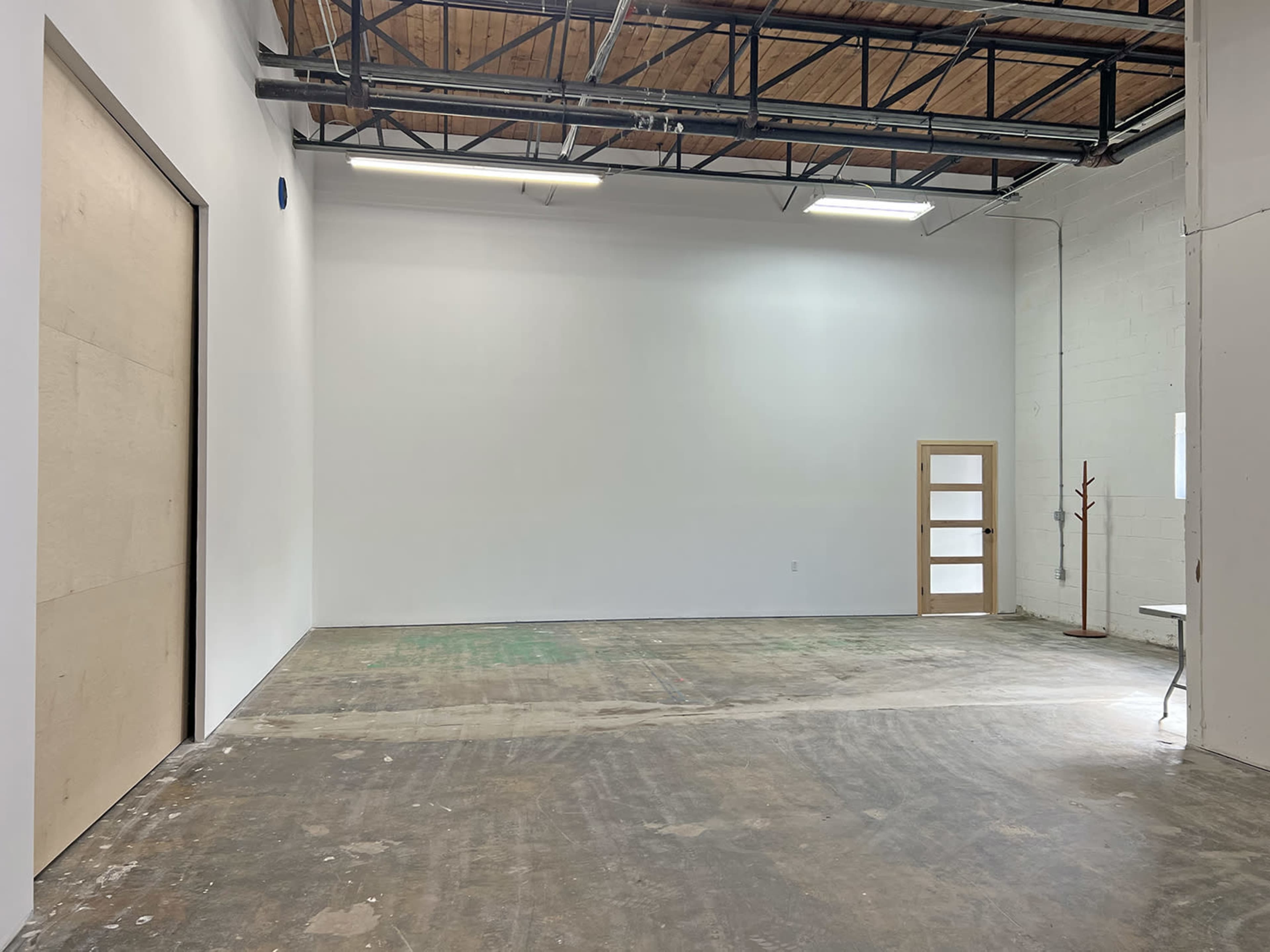 A spacious, empty interior with concrete flooring, tall ceilings, and a large wall featuring a door and a window.