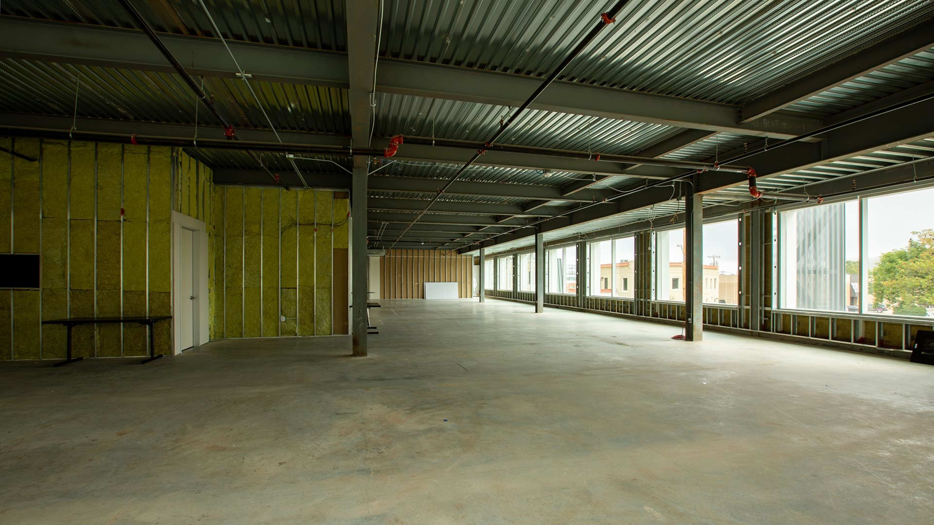 An empty, under-construction commercial space with exposed steel beams and large windows.