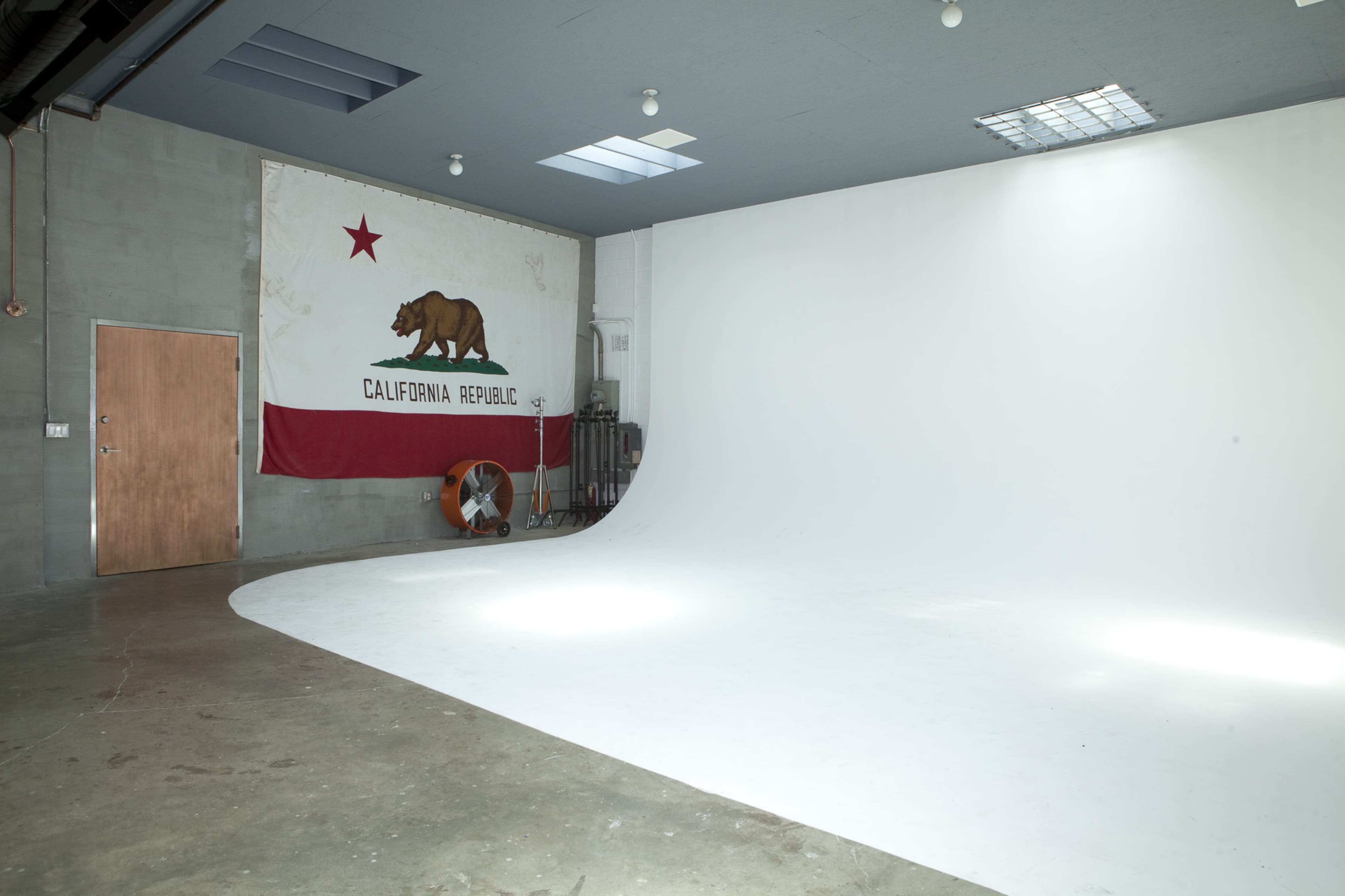 An empty studio space with a curved white backdrop and a California state flag on the wall.