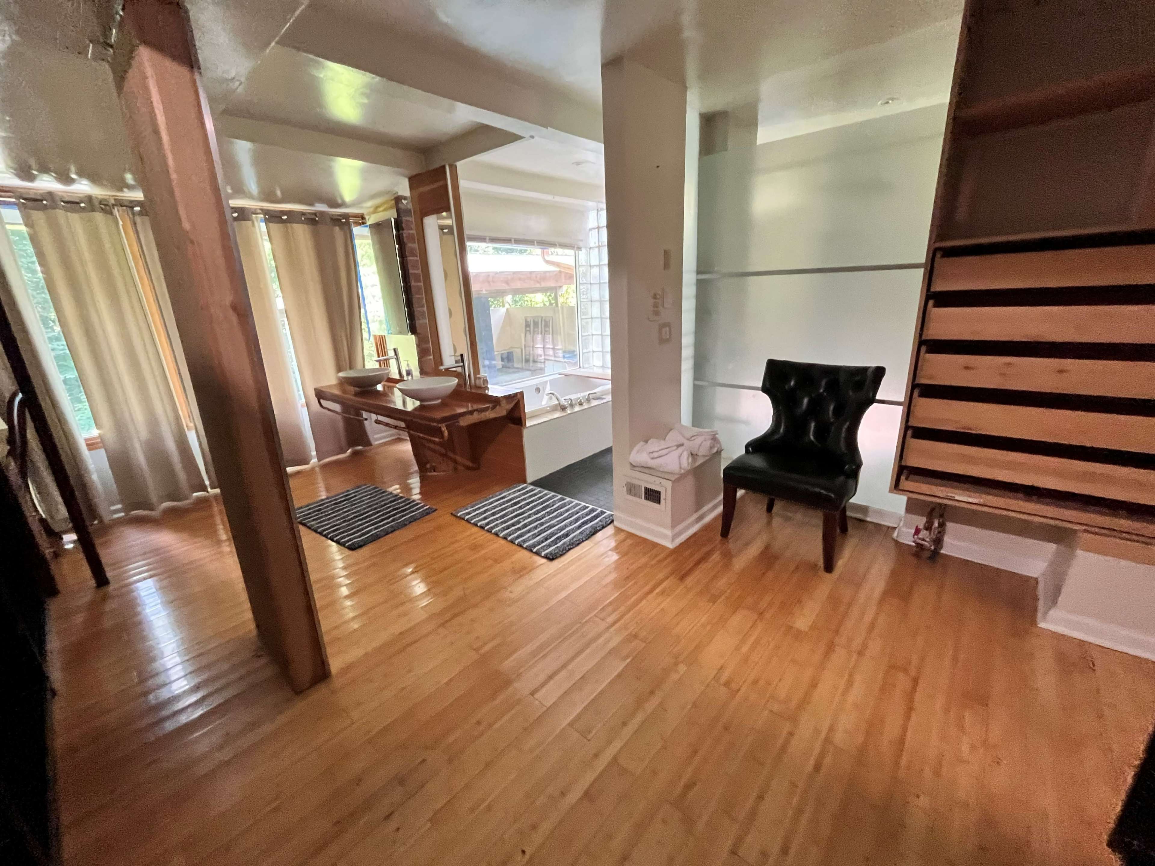 A well-lit open space featuring a wooden floor, a chair, a vanity area with a sink, and a view into a bathroom area with a tub.