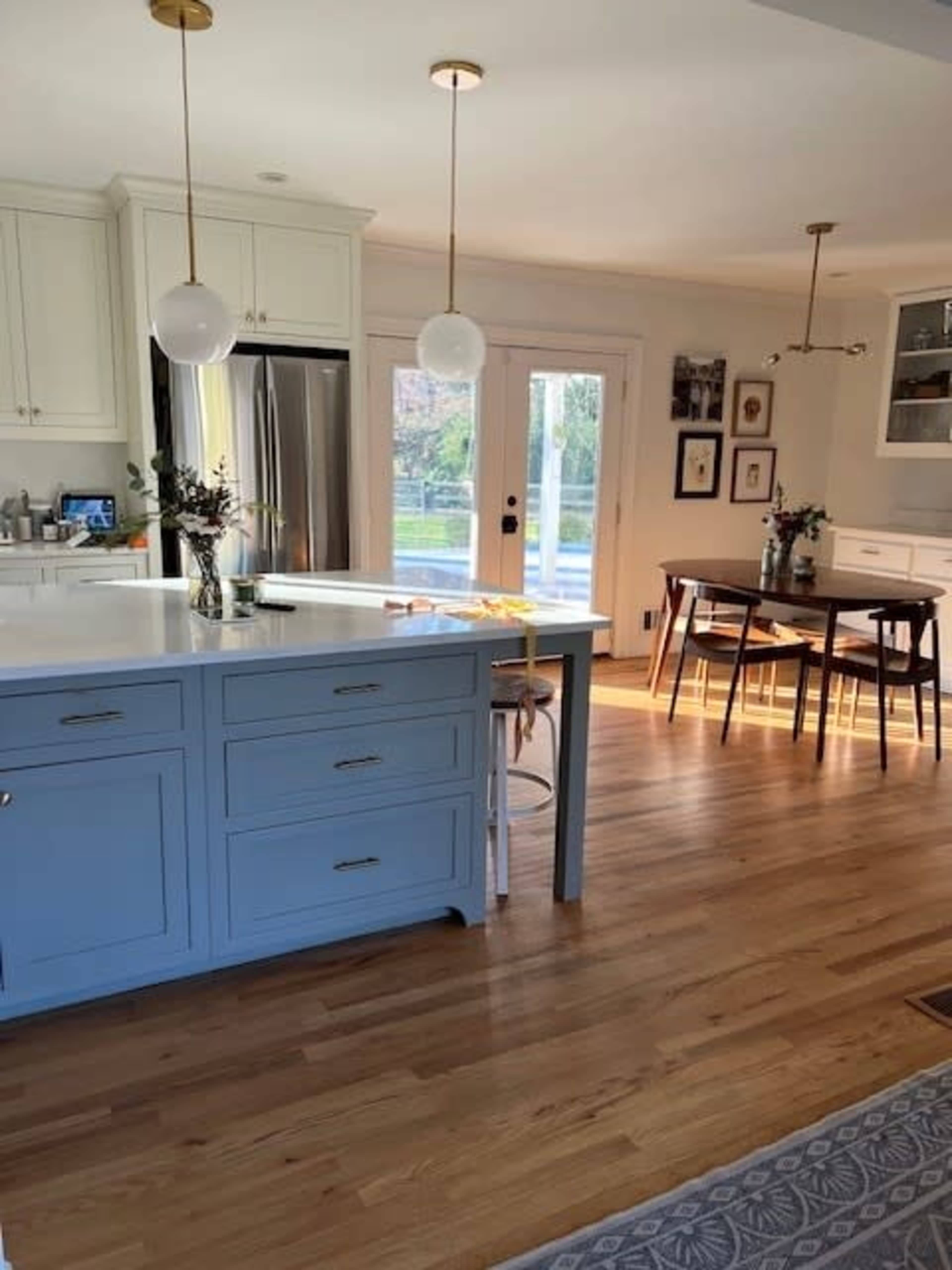 A bright, modern kitchen features a blue island, stainless steel appliances, and a dining area with a wooden table and chairs.