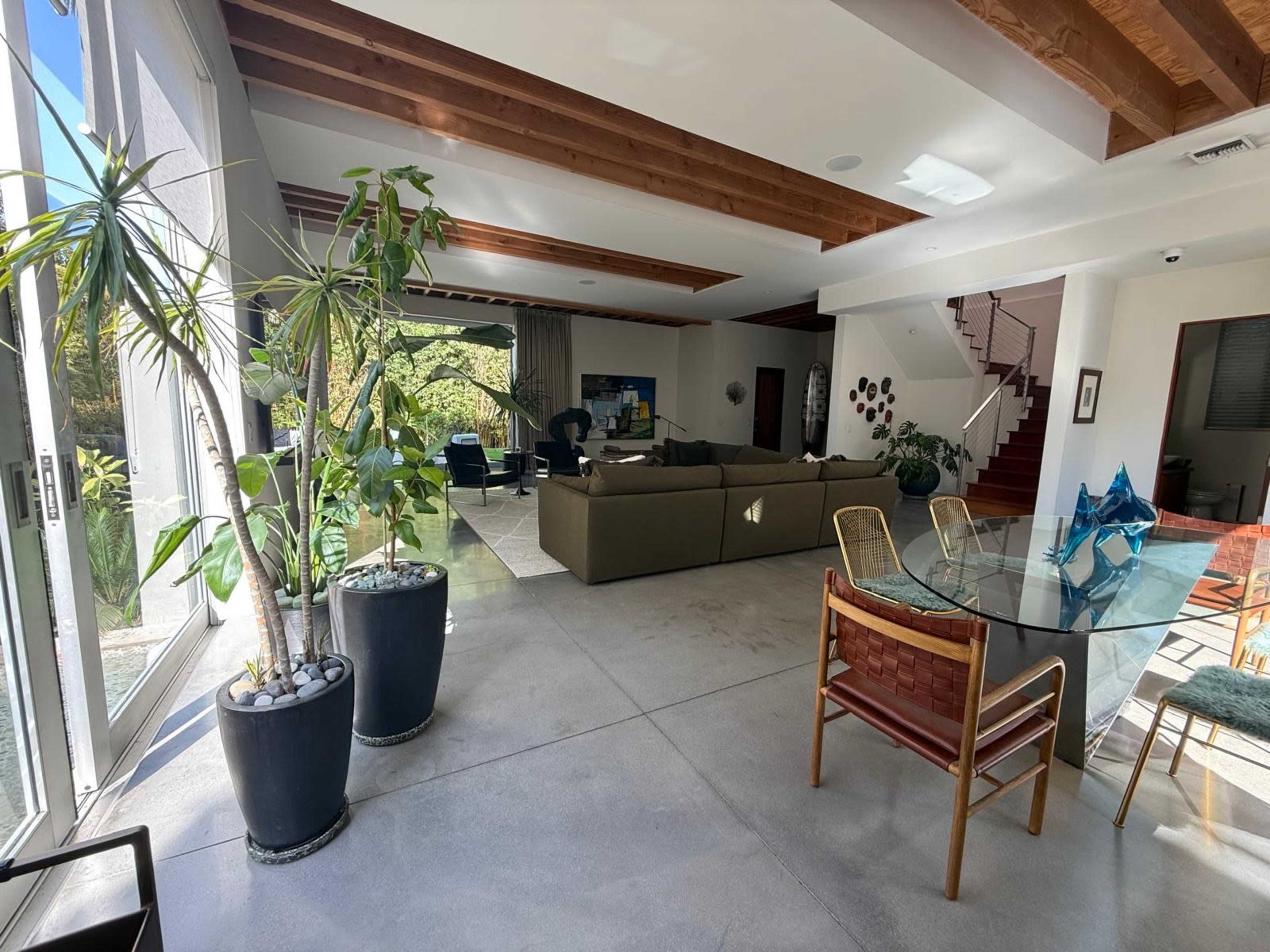 A spacious living area features large windows, a sectional sofa, and a dining table surrounded by chairs.