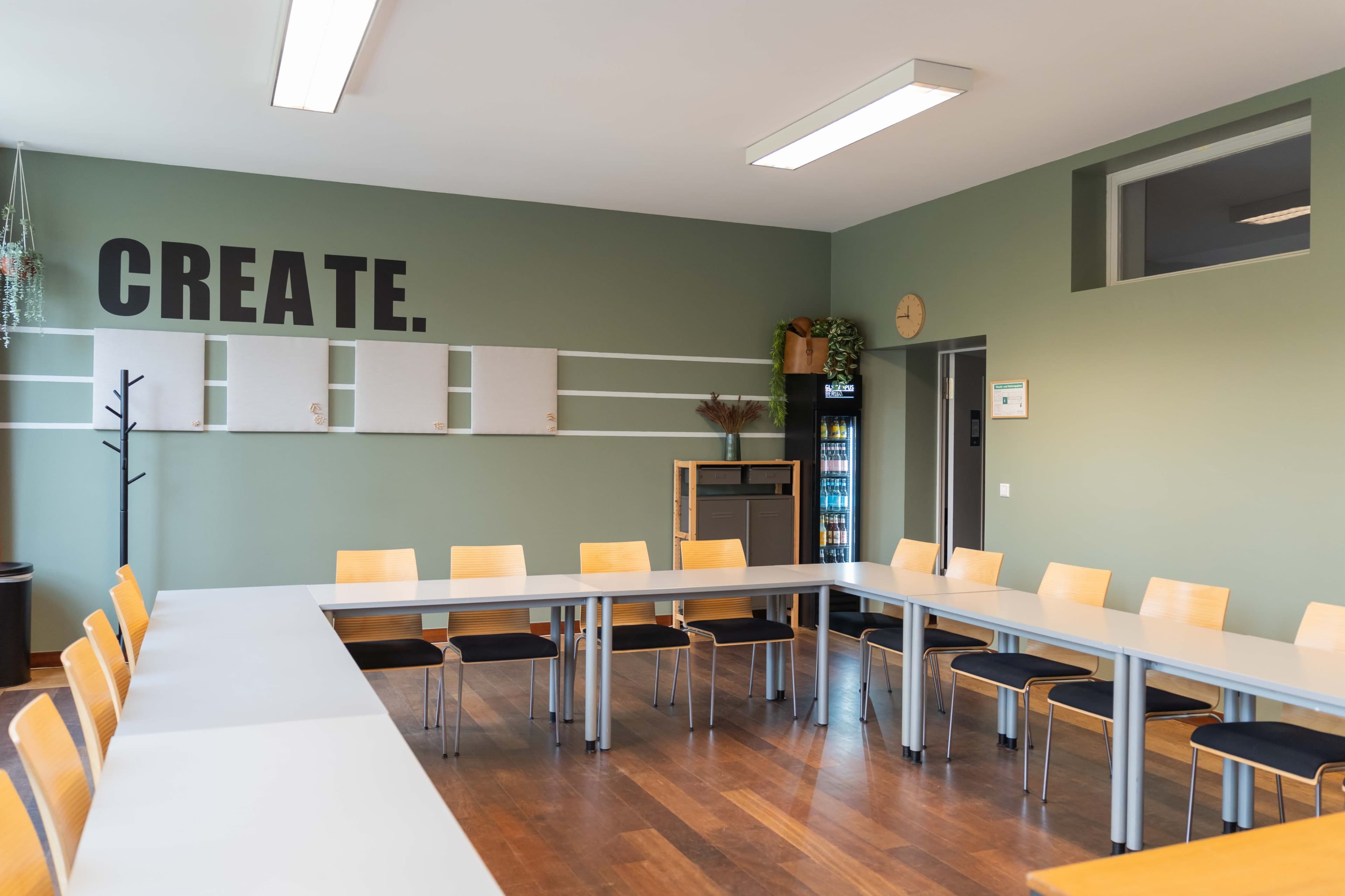 The image shows a meeting room with a large rectangular table surrounded by wooden chairs, featuring a wall with the word "CREATE" in bold letters.