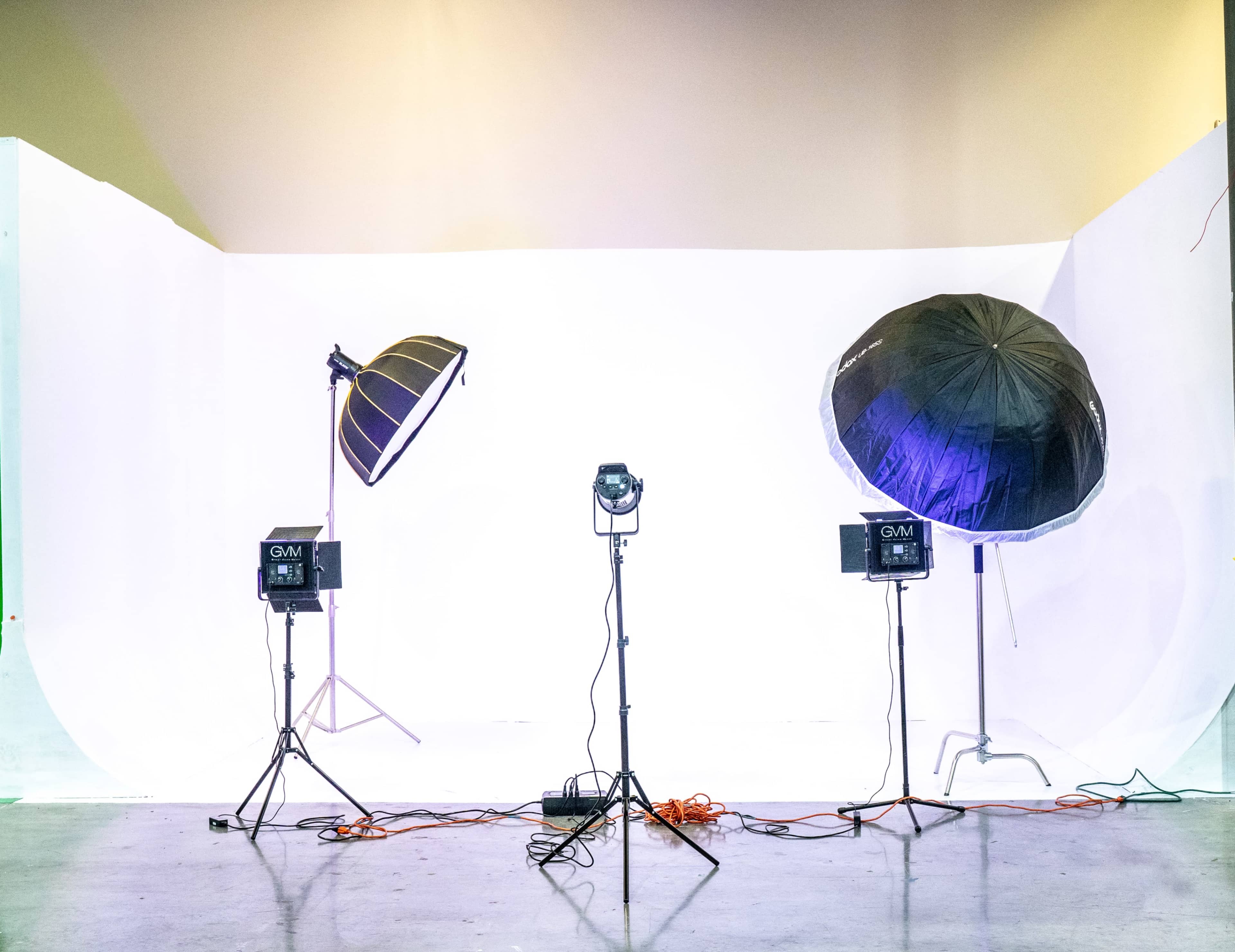A photography studio setup features two large softbox lights and multiple light fixtures on a white backdrop.