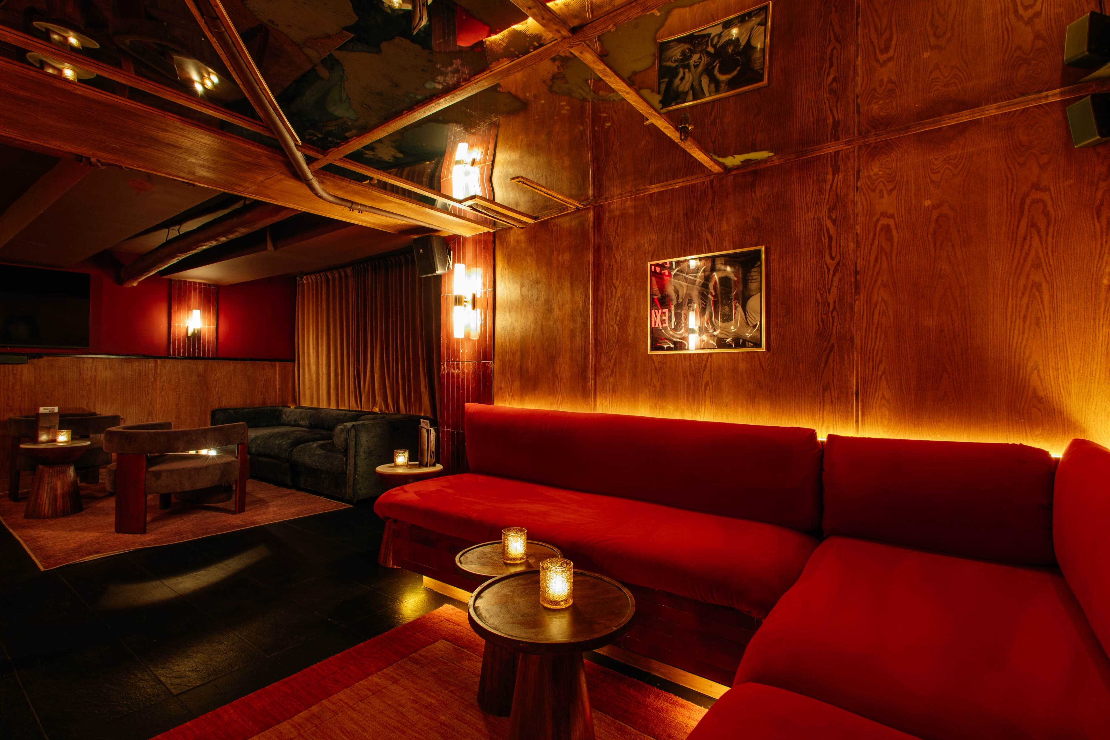 The image shows a dimly lit lounge with red sofas, wooden walls, and small tables with candles.