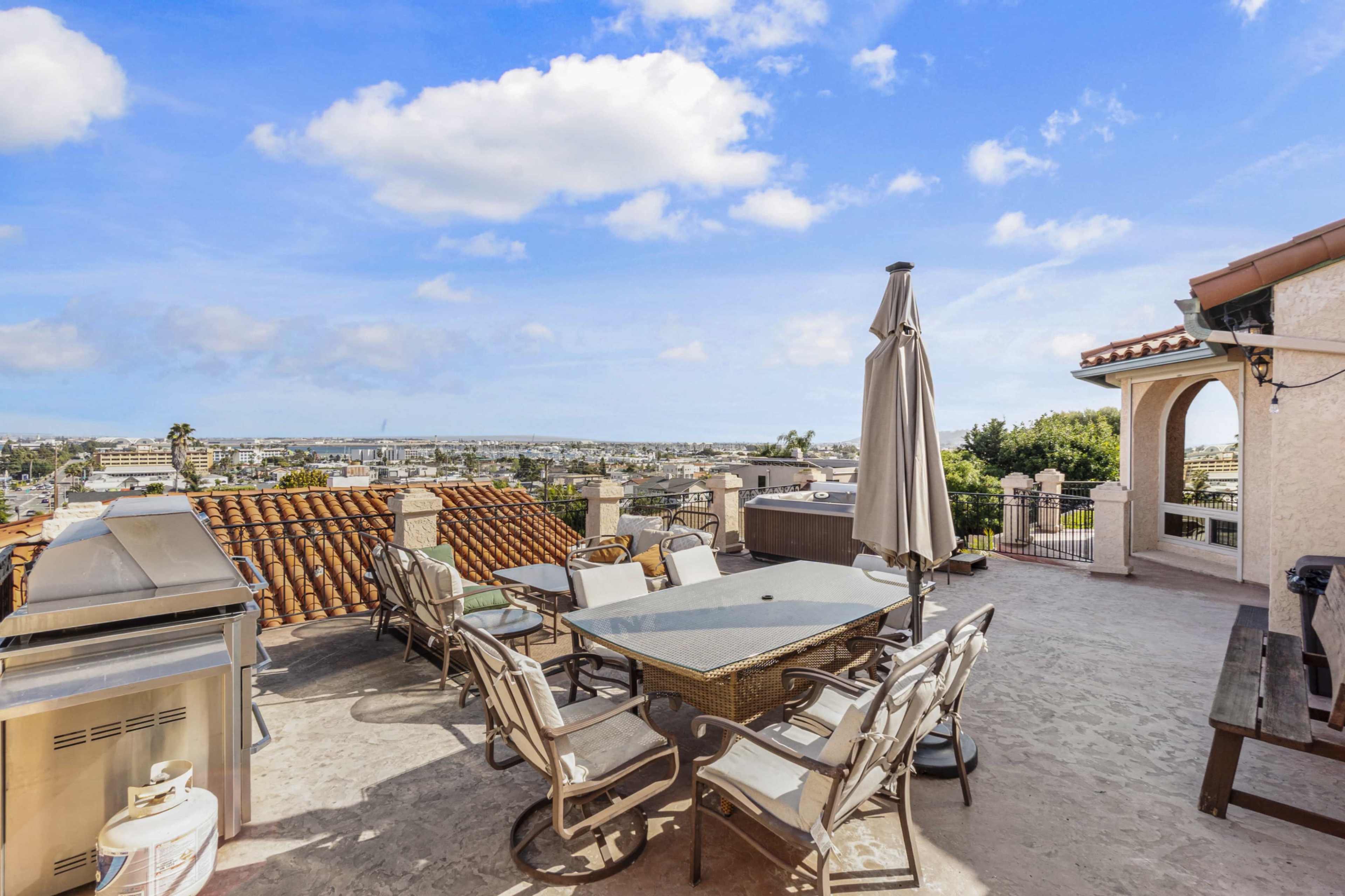 A spacious rooftop terrace features a dining table, seating area, and a grill with a panoramic view of the surrounding landscape.