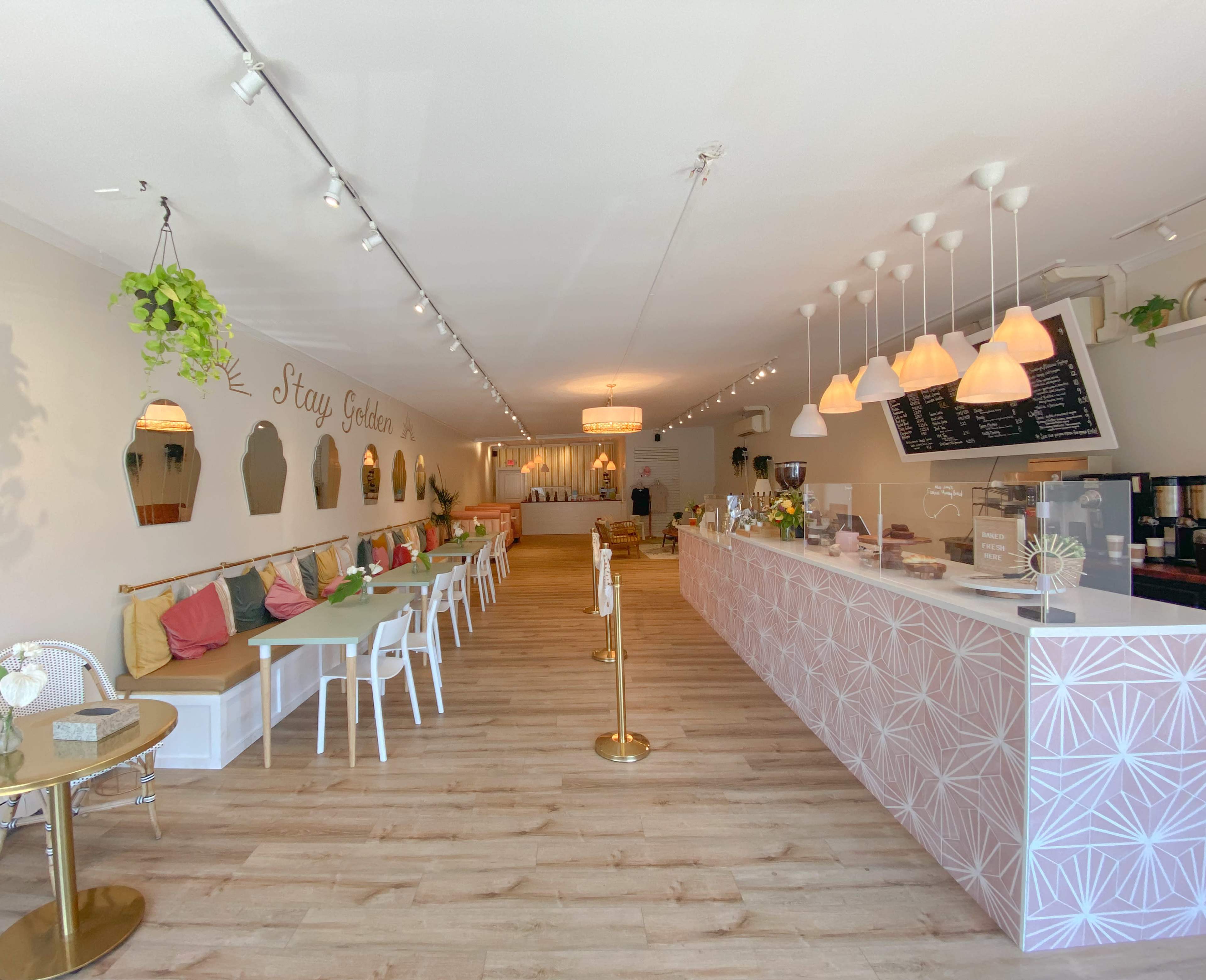 A modern café interior featuring a long counter with a menu display, seating areas with colorful cushions, and decorative elements on the walls.