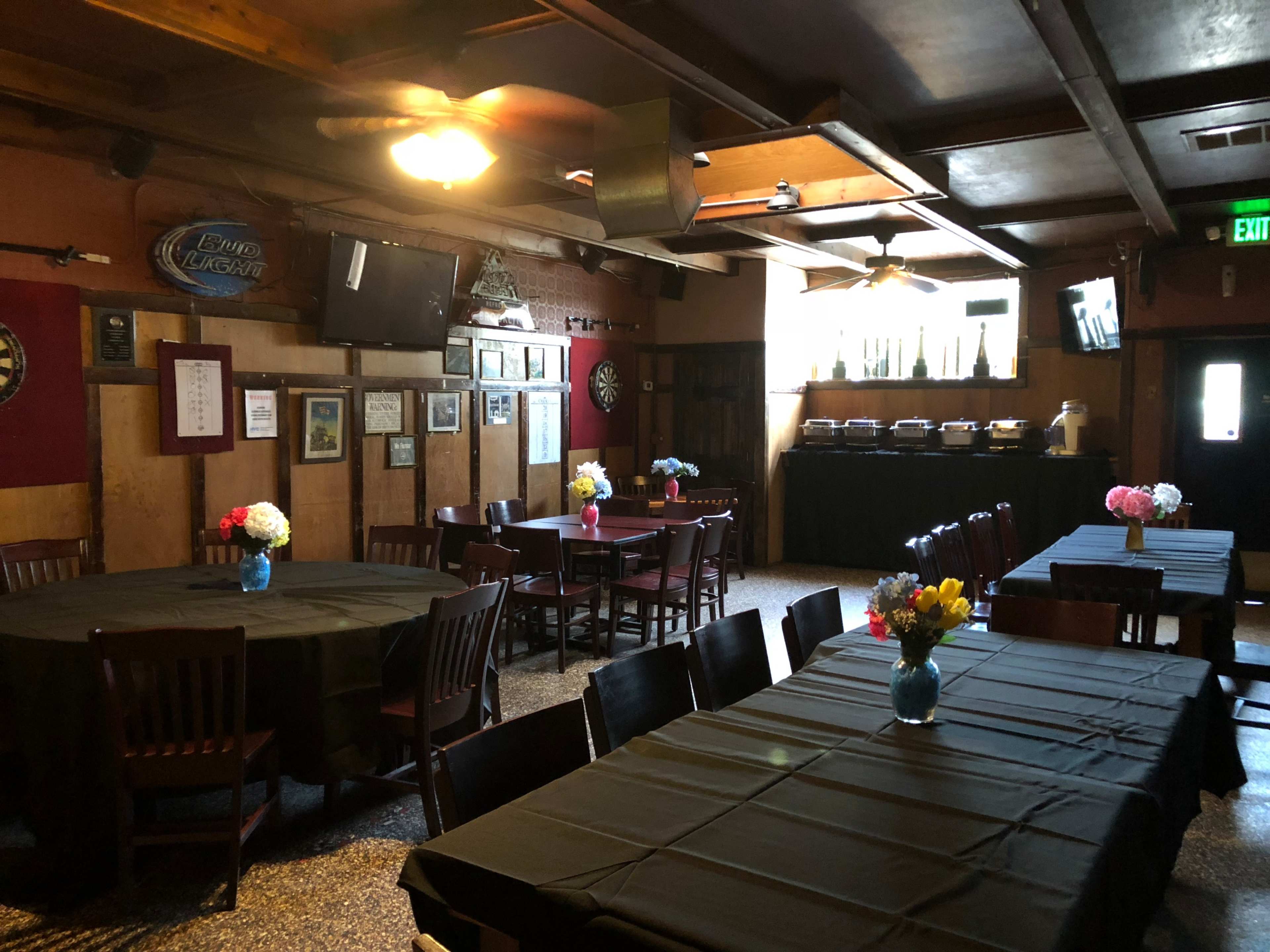 A spacious dining area features multiple tables with black tablecloths and colorful floral centerpieces, along with a buffet setup in the background.
